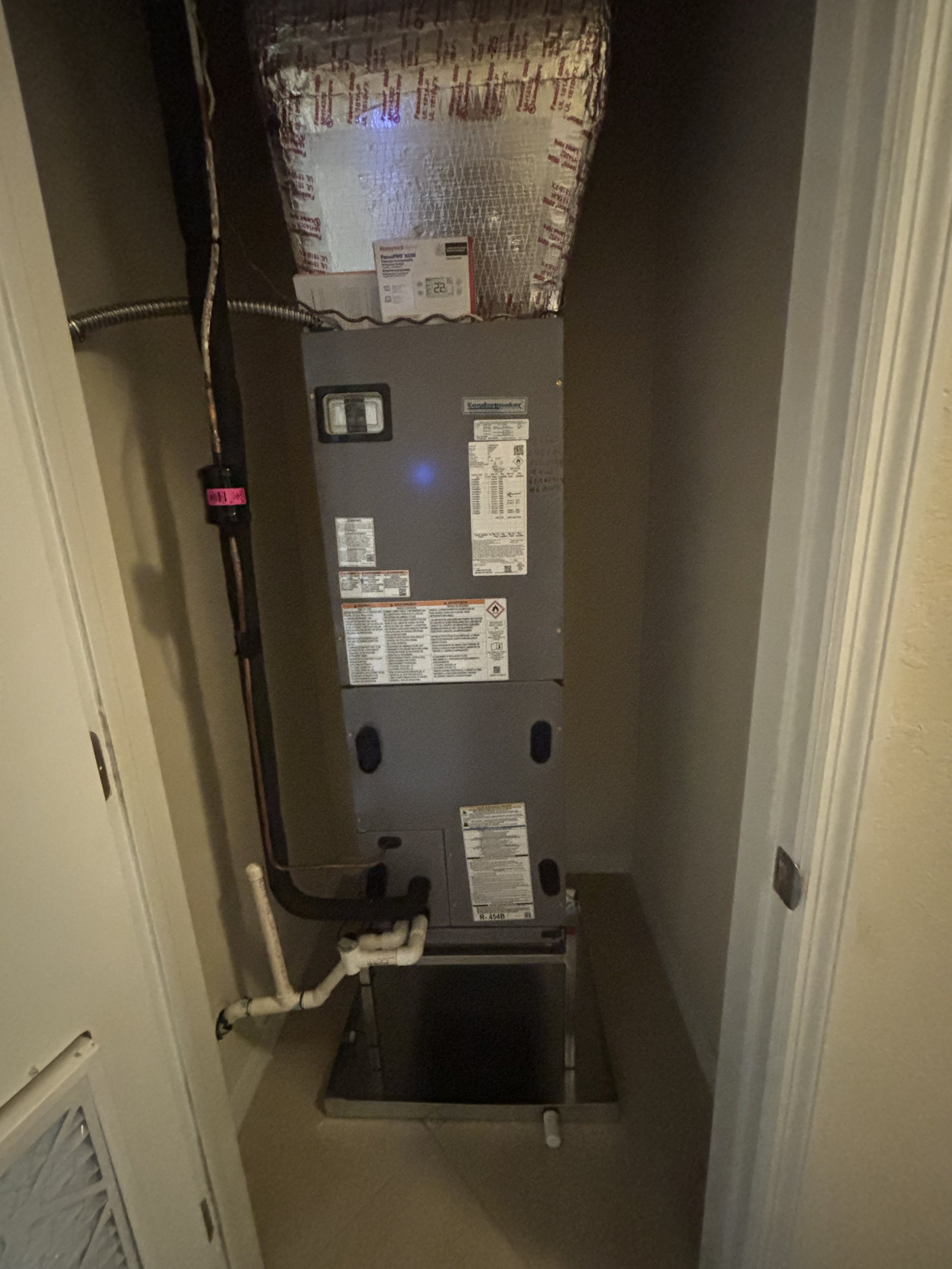 Furnace or HVAC unit installed in a closet with a metal duct connected at the top and pipes at the bottom.