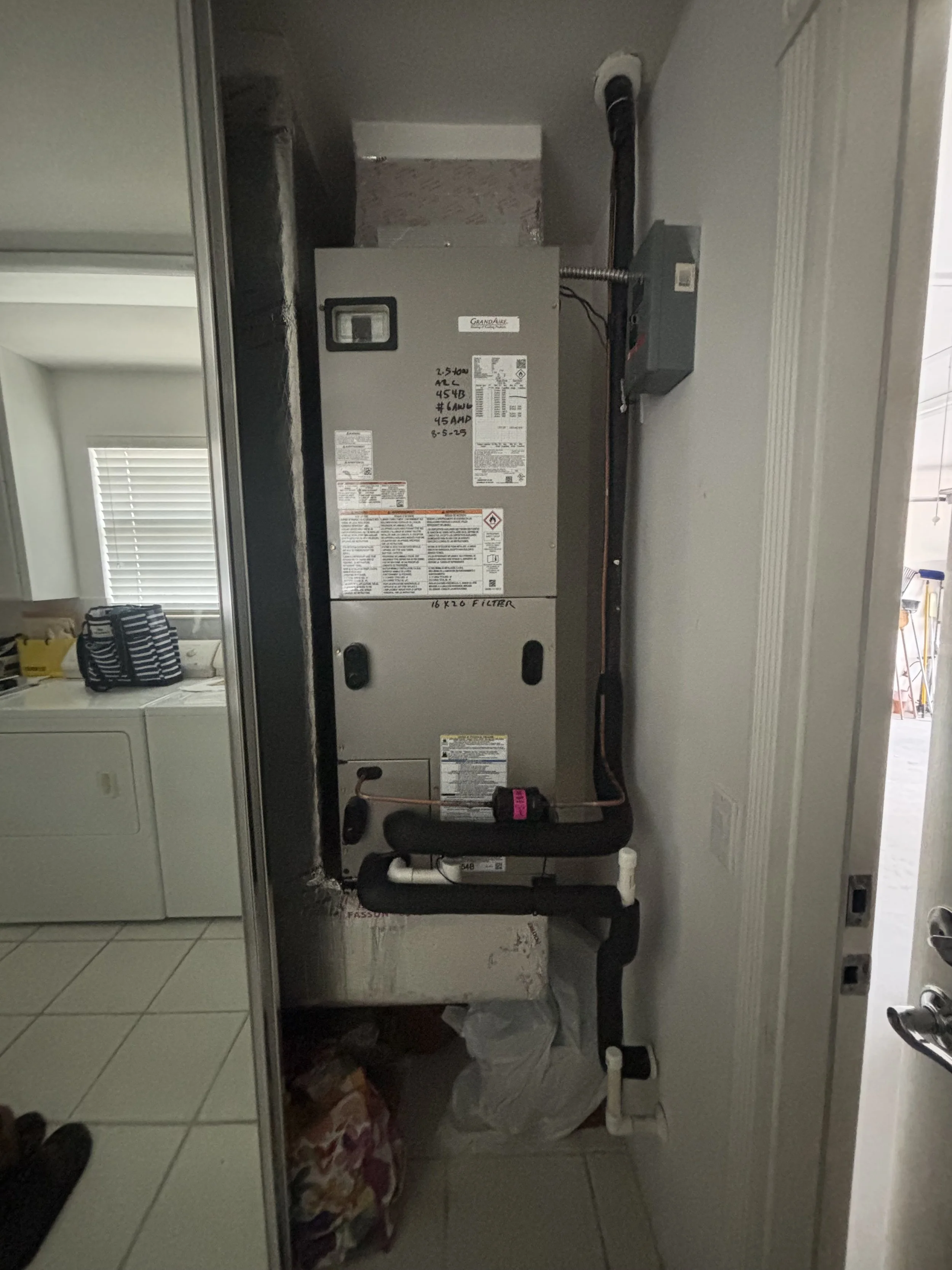 A view of a AH unit installed in a laundry room, with pipes and electrical connections visible, next to a door and a sidewall.