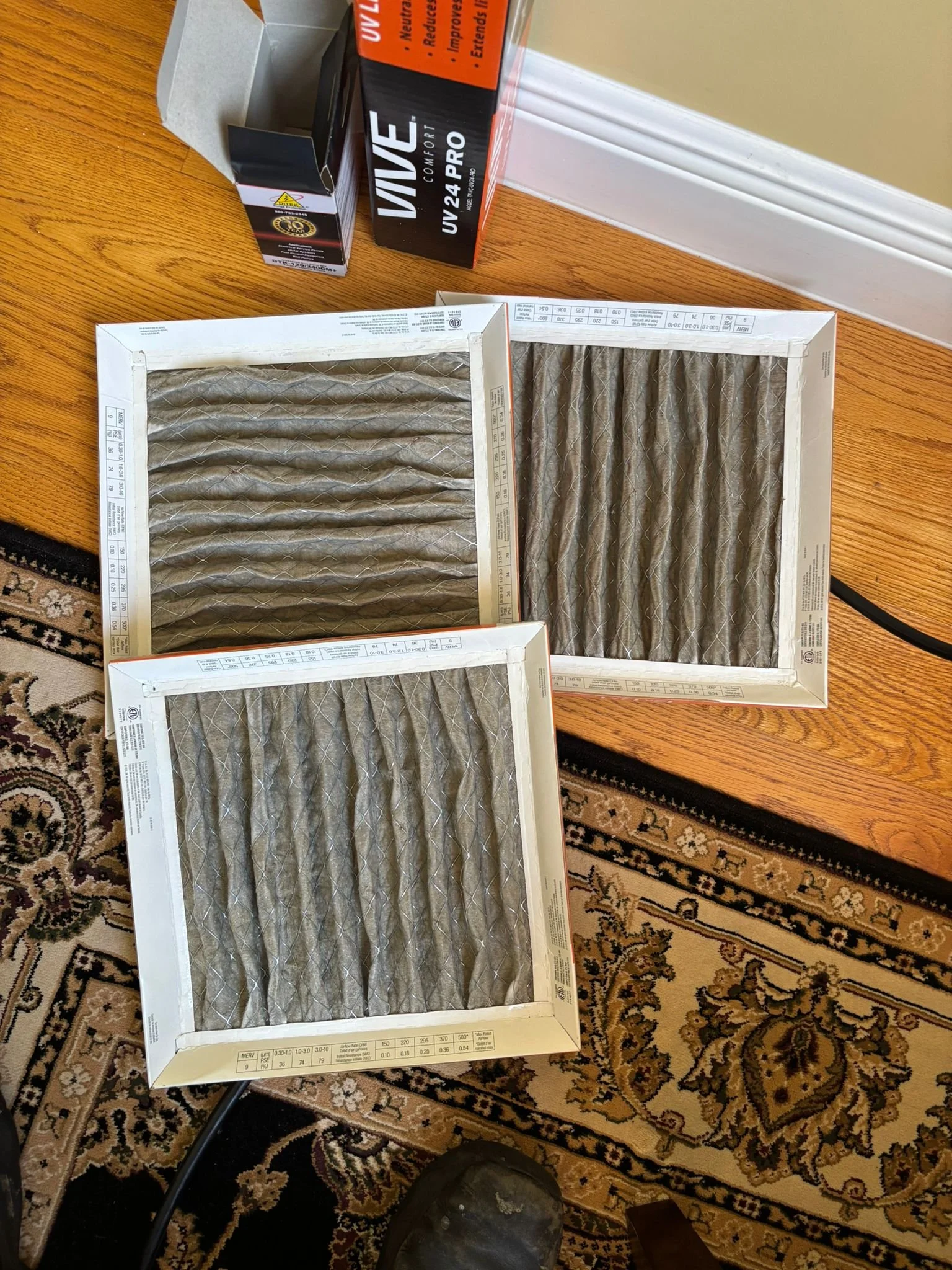 Three used HVAC air filters placed on a wooden table, with boxes of UV protection lamps beside them.