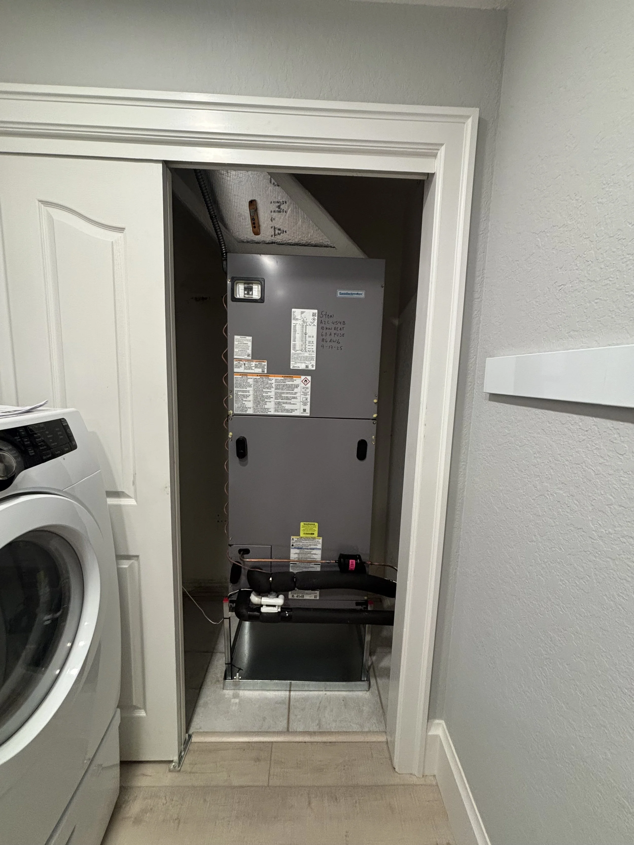 An HVAC furnace installed in a small closet next to a laundry washing machine.