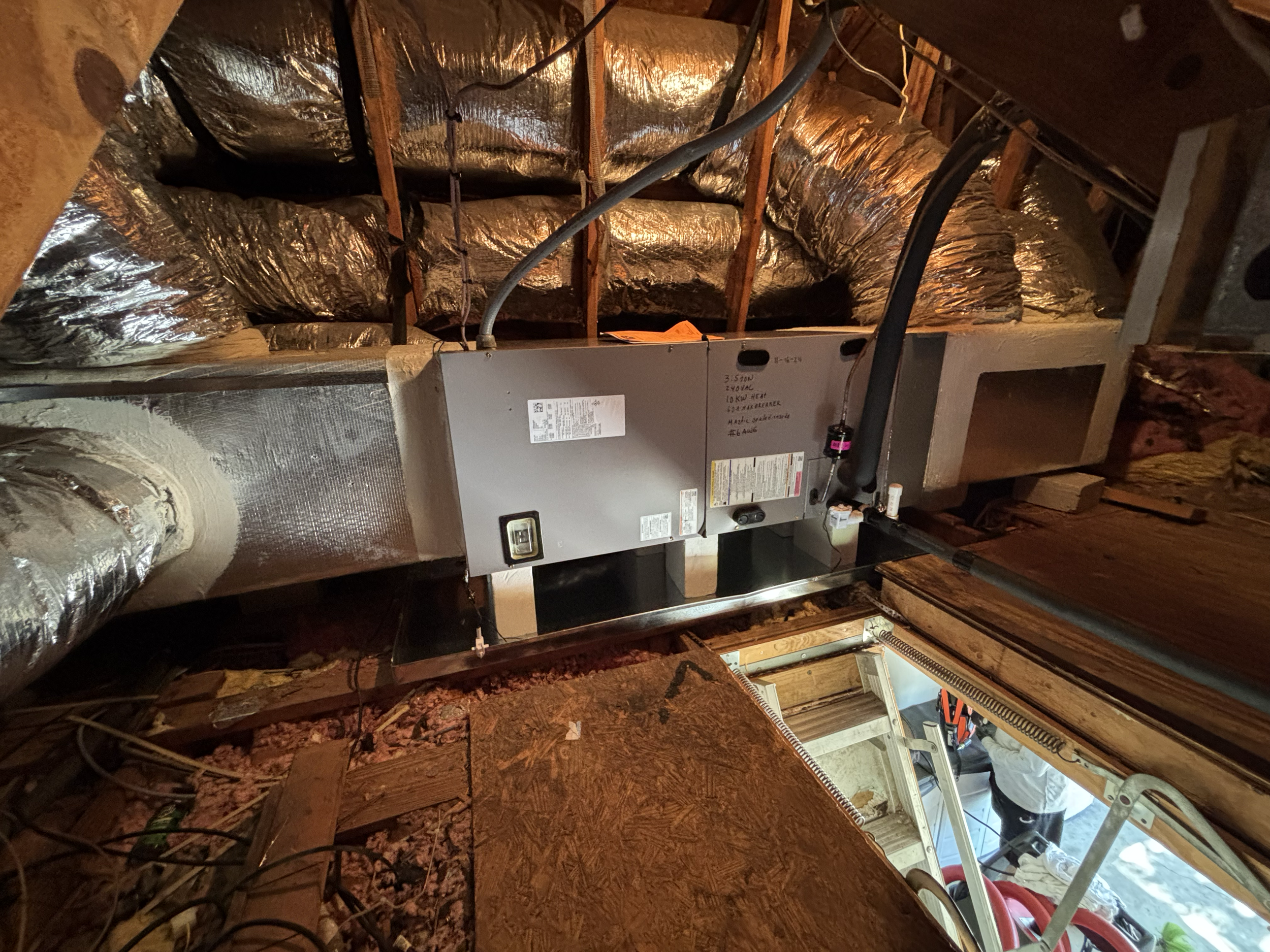 An HVAC system installation in an attic with ductwork, insulation, and construction materials visible.