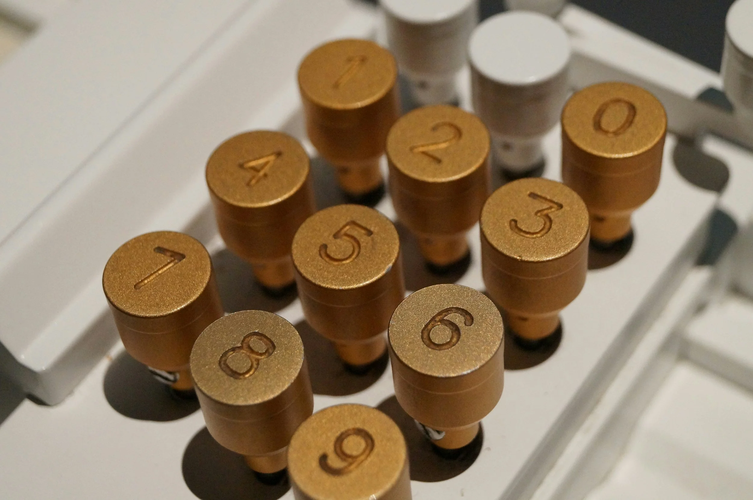 Close-up of a vintage typewriter keyboard showing the top of round, gold-colored keys with black numbers from 1 to 9 and 0 engraved, arranged in a QWERTY layout.