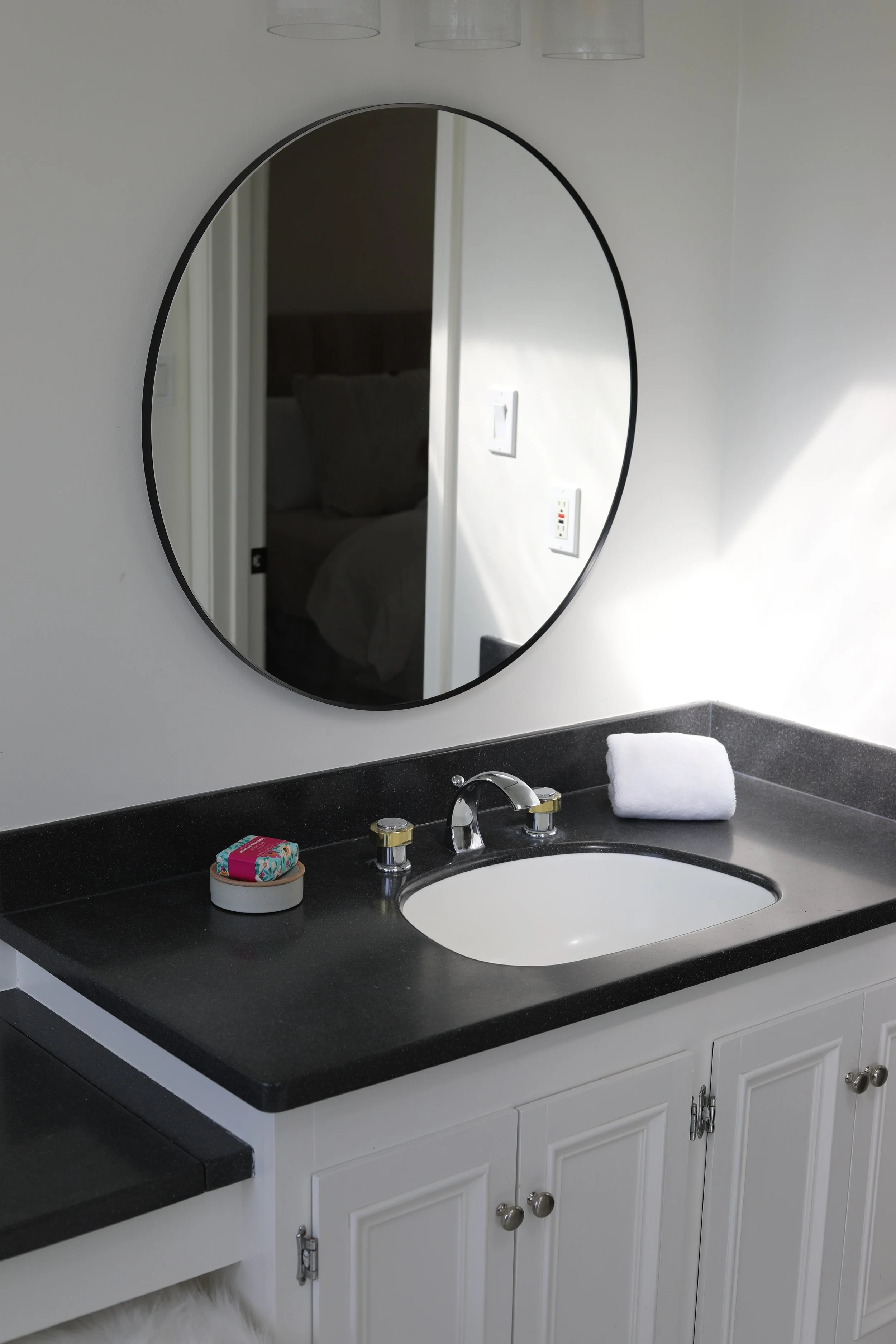 Bathroom vanity with a black countertop, a white sink, a mirror above, a rolled white towel, and soap on a small dish.