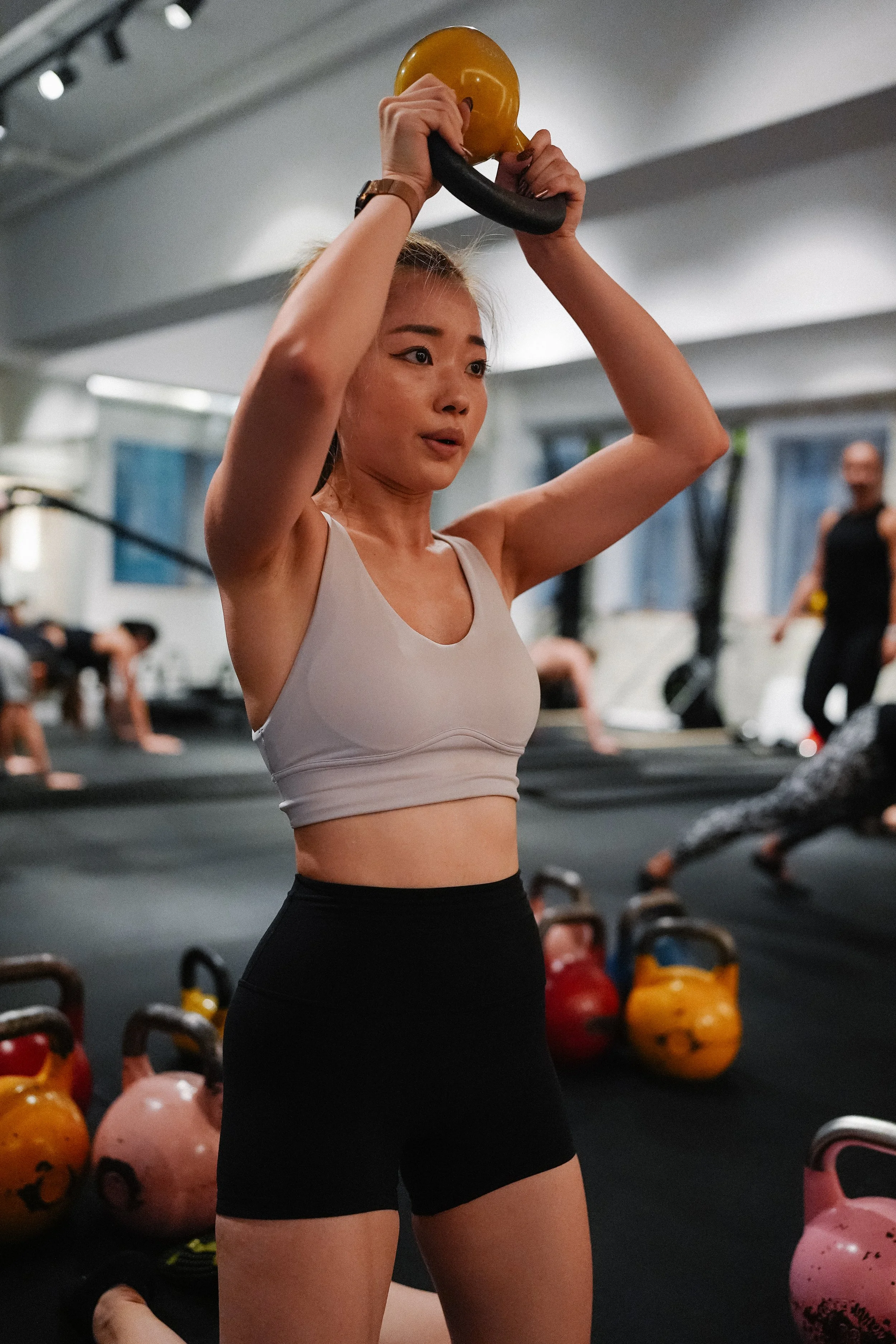 A woman in workout attire lifting a kettlebell in a gym.