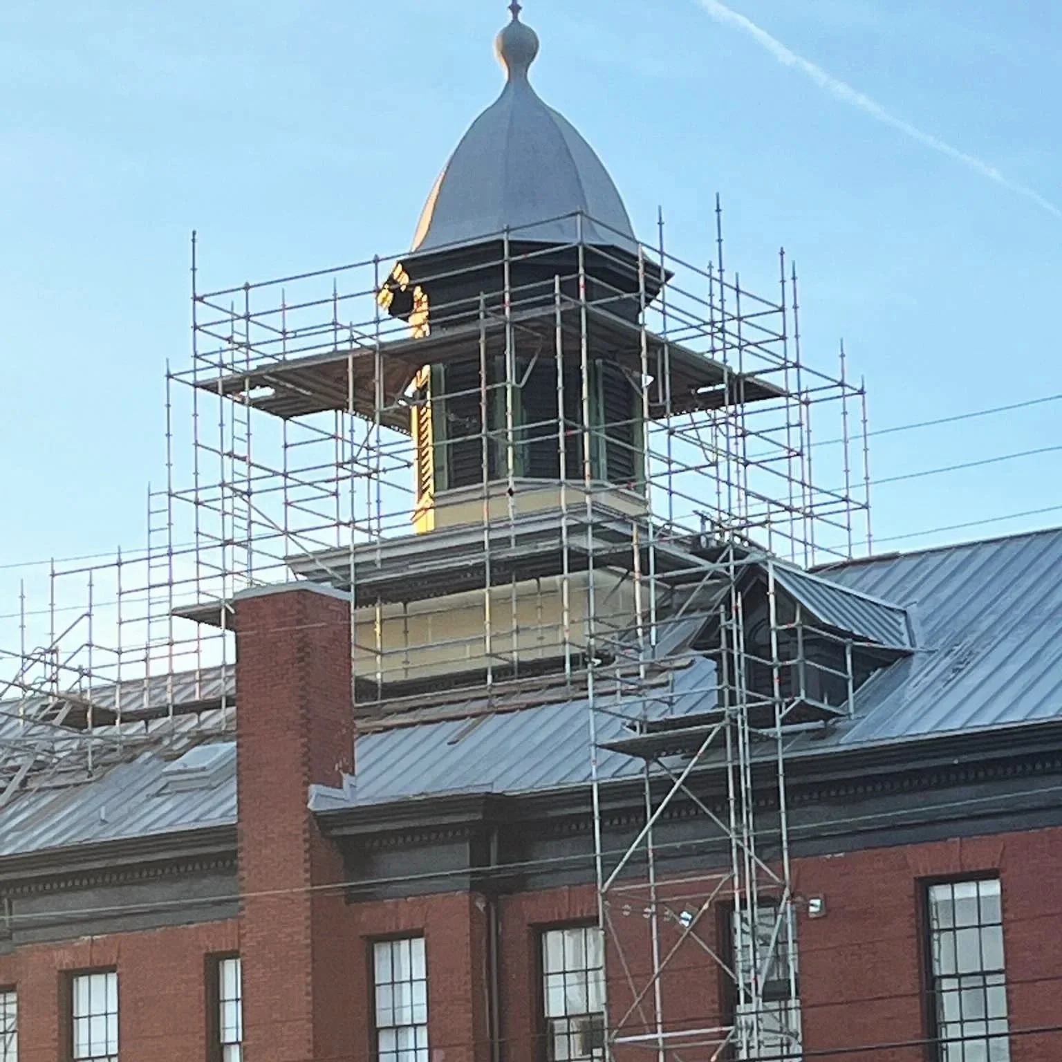 Scaffolding surrounding the clock tower of a brick building with a mansard roof, during daytime.