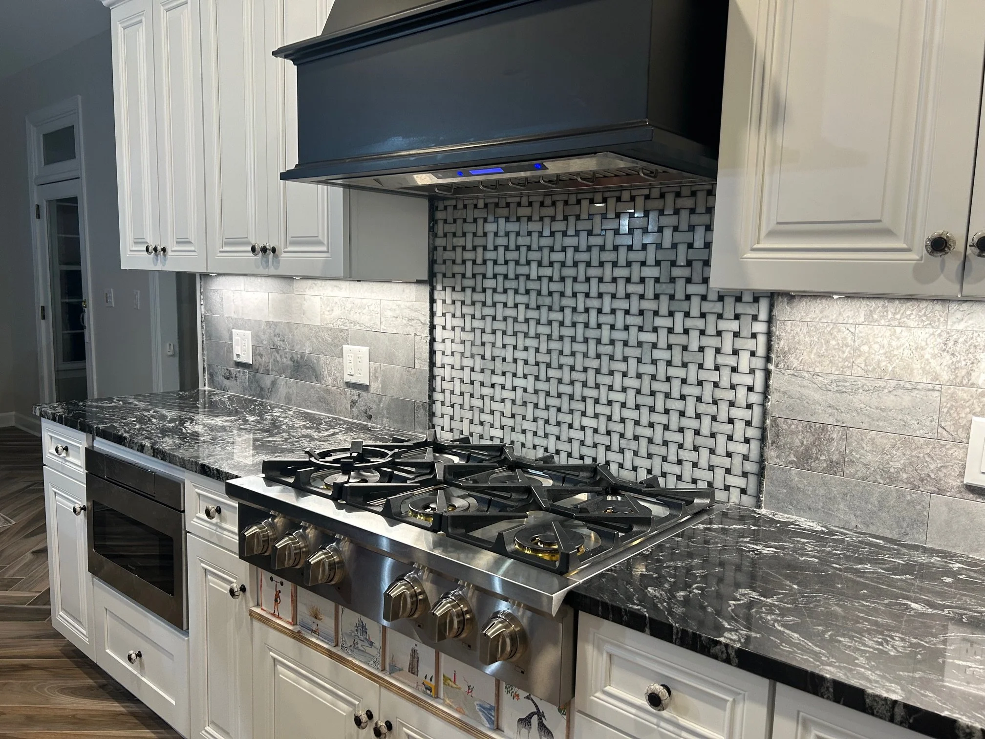 Kitchen with white cabinetry, a black stove with four burners, a decorative tile backsplash in gray and white, and a marble countertop with black and white veining.