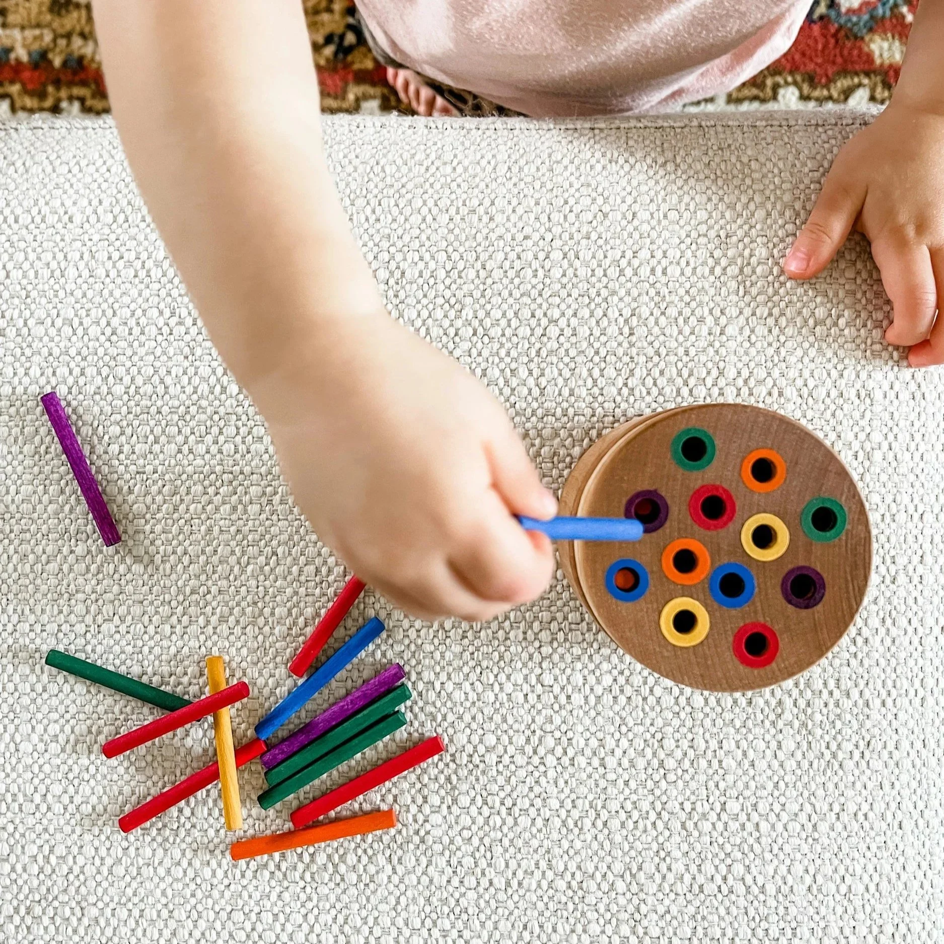 Child playing with colorful Dr. Seuss-themed lacing beads and sticks on a beige textured surface.