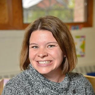A woman with shoulder-length brown hair smiling in a classroom setting.