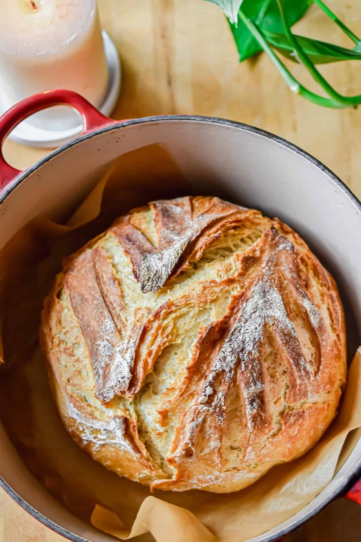 Round, rustic bread with a dusting of flour on top, resting inside a baking pot lined with parchment paper.