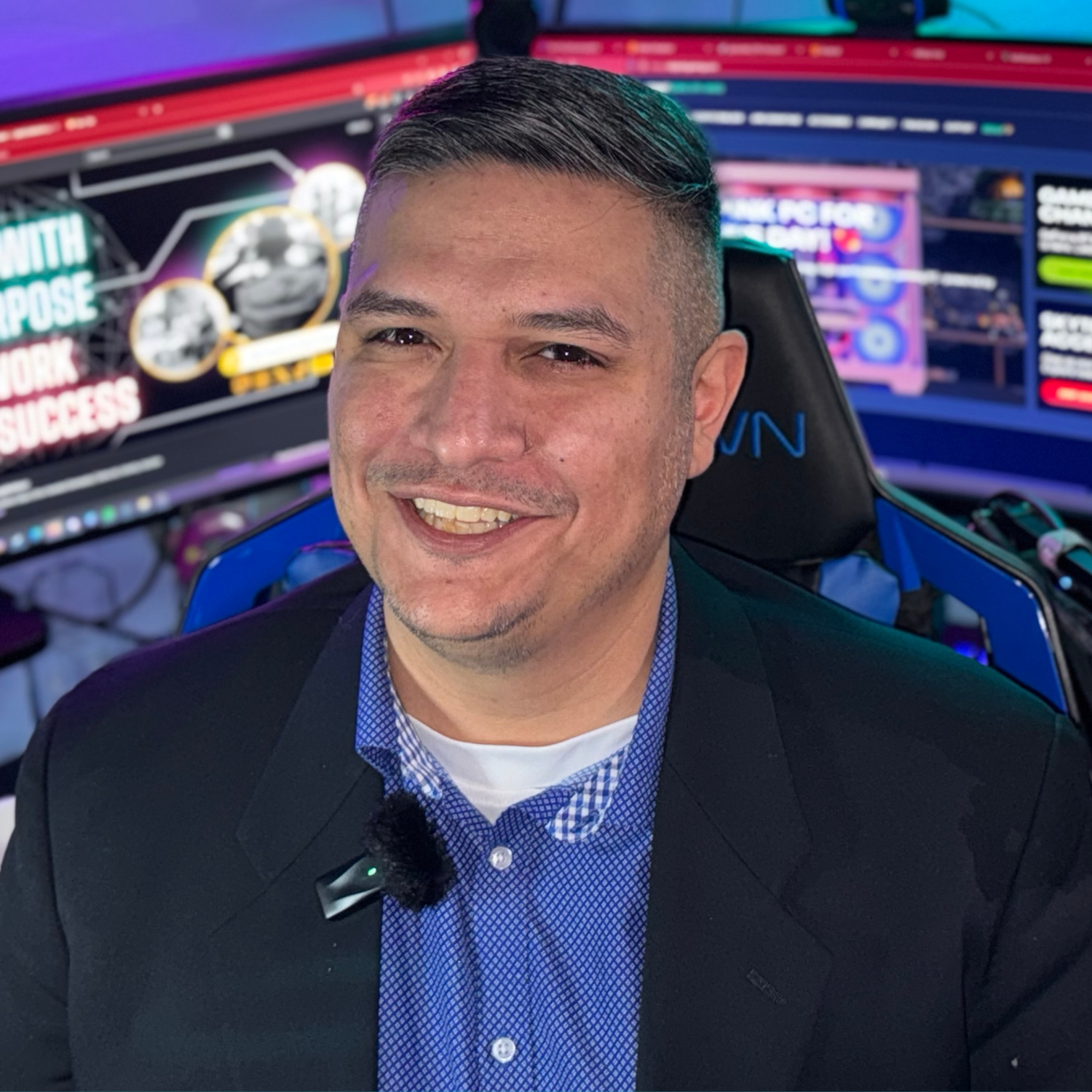 A smiling man in a business suit sitting in front of multiple computer screens with colorful graphics.