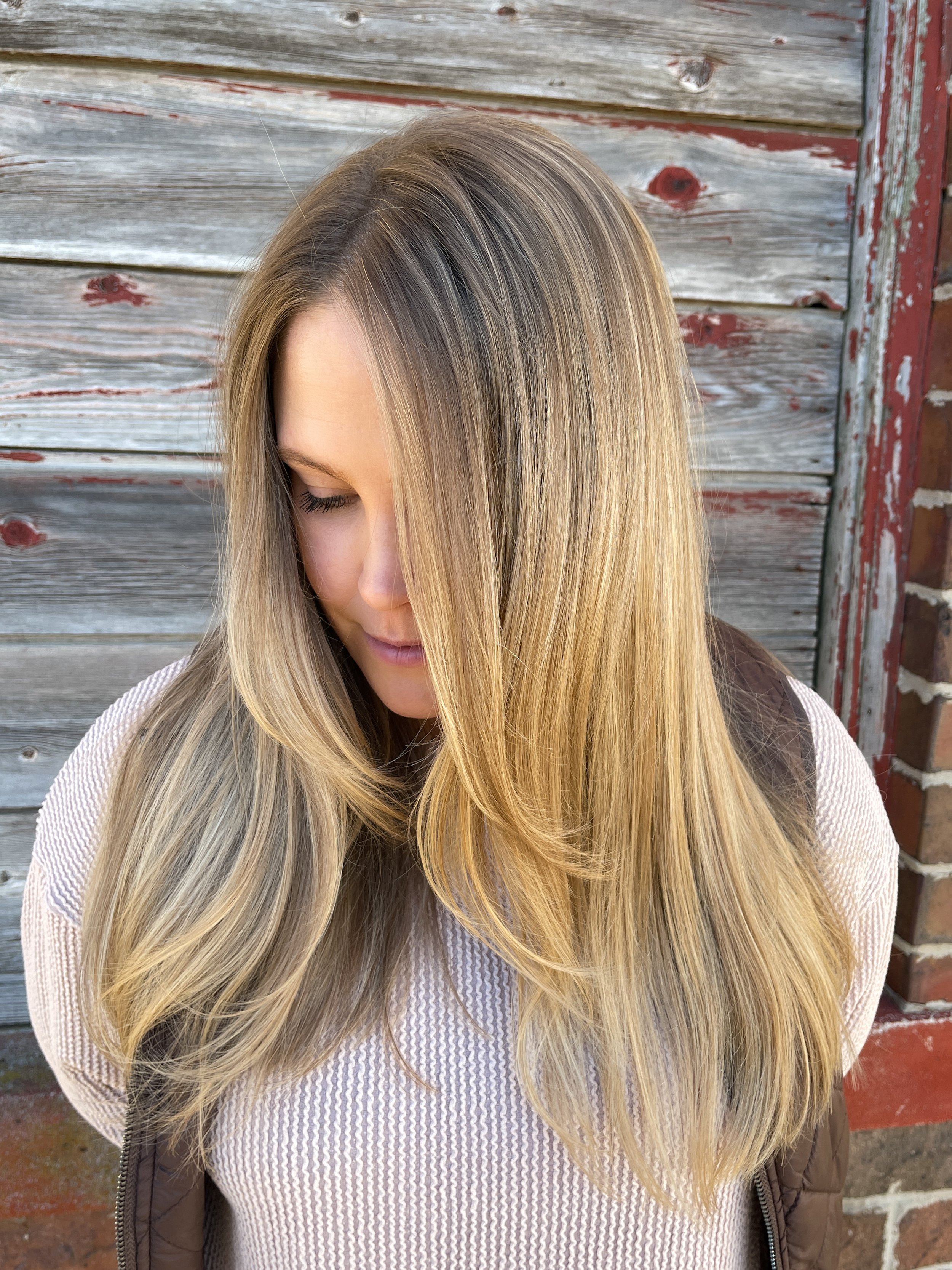 Close-up of a woman with long, straight blonde hair looking down against a weathered wooden fence background.