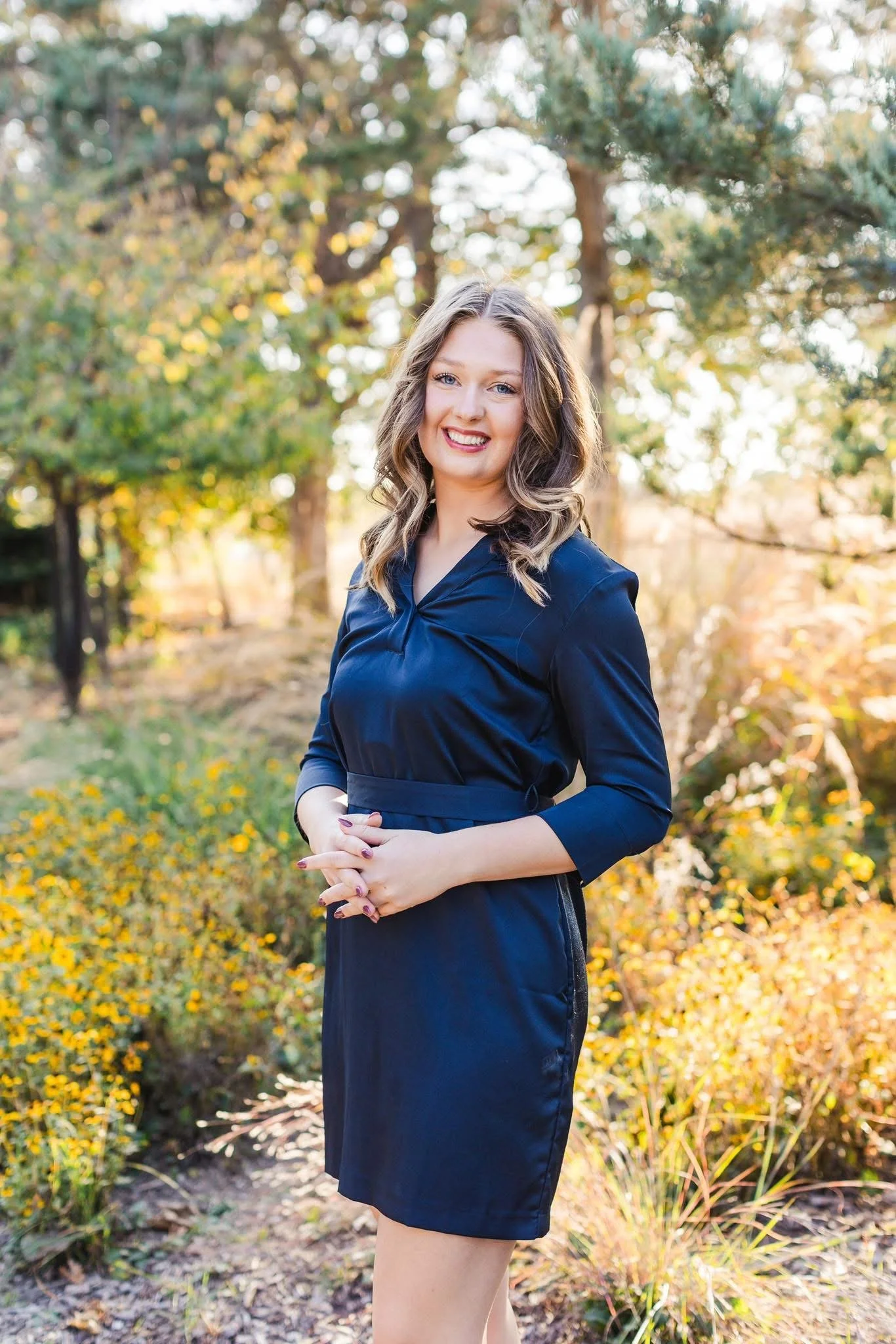 A young woman with with collarbone-length curled hair, smiling in an outdoor setting