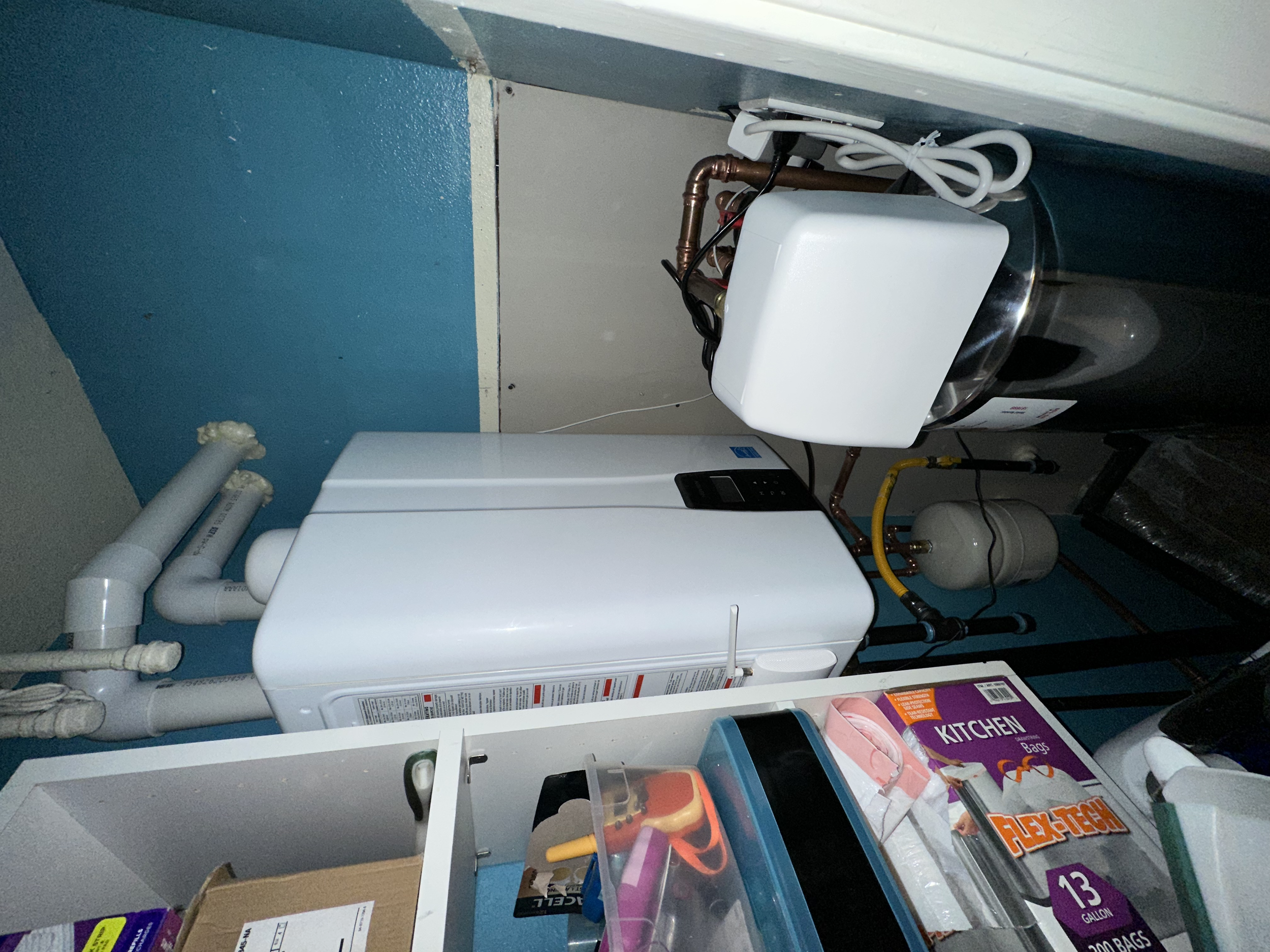 A Navien NPE-240 tankless water heater. A laundry room with a washing machine, water heater, and various supplies and boxes on shelves.