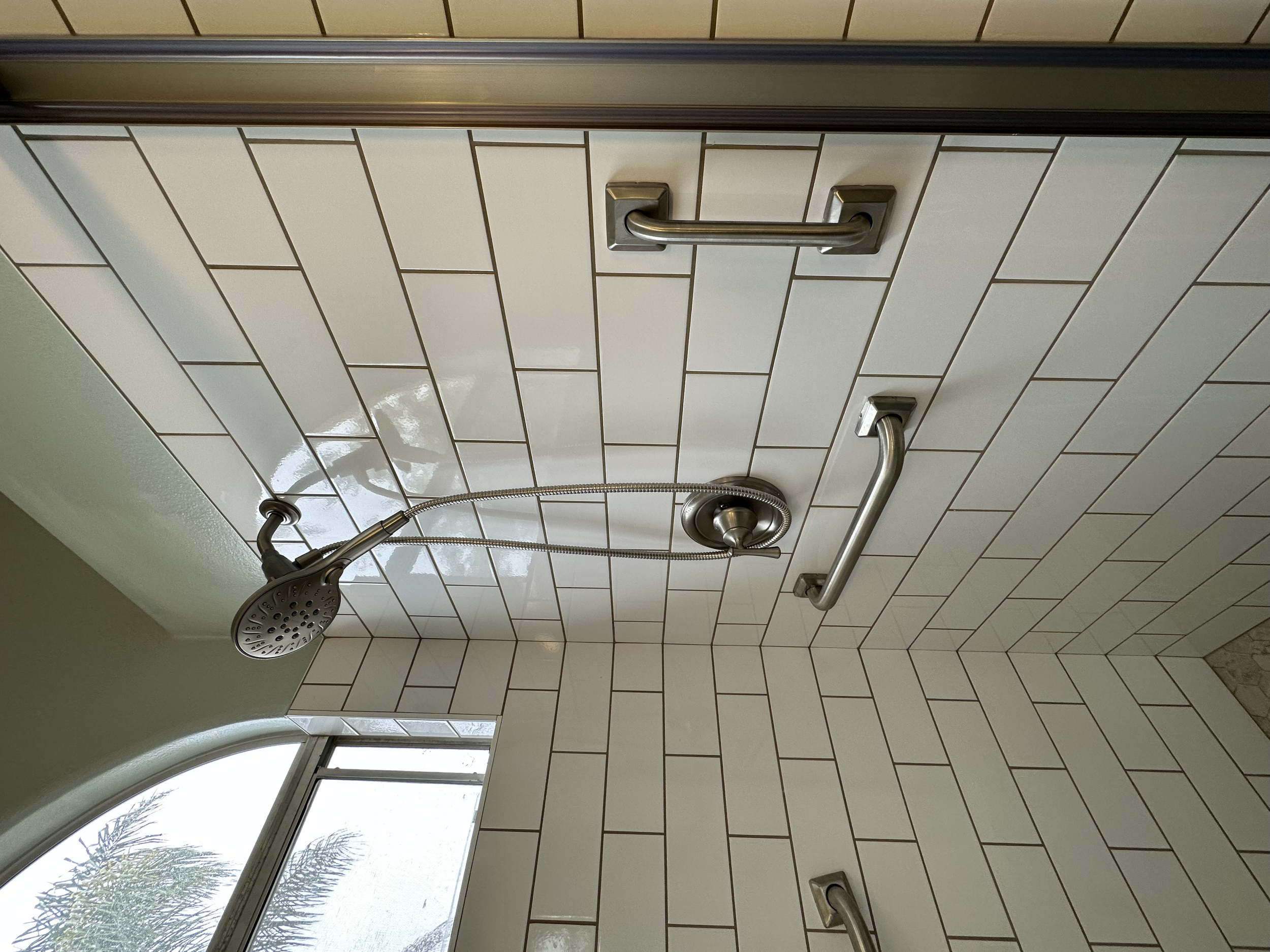 Shower area with white tiled walls, a handheld showerhead, and grab bars.