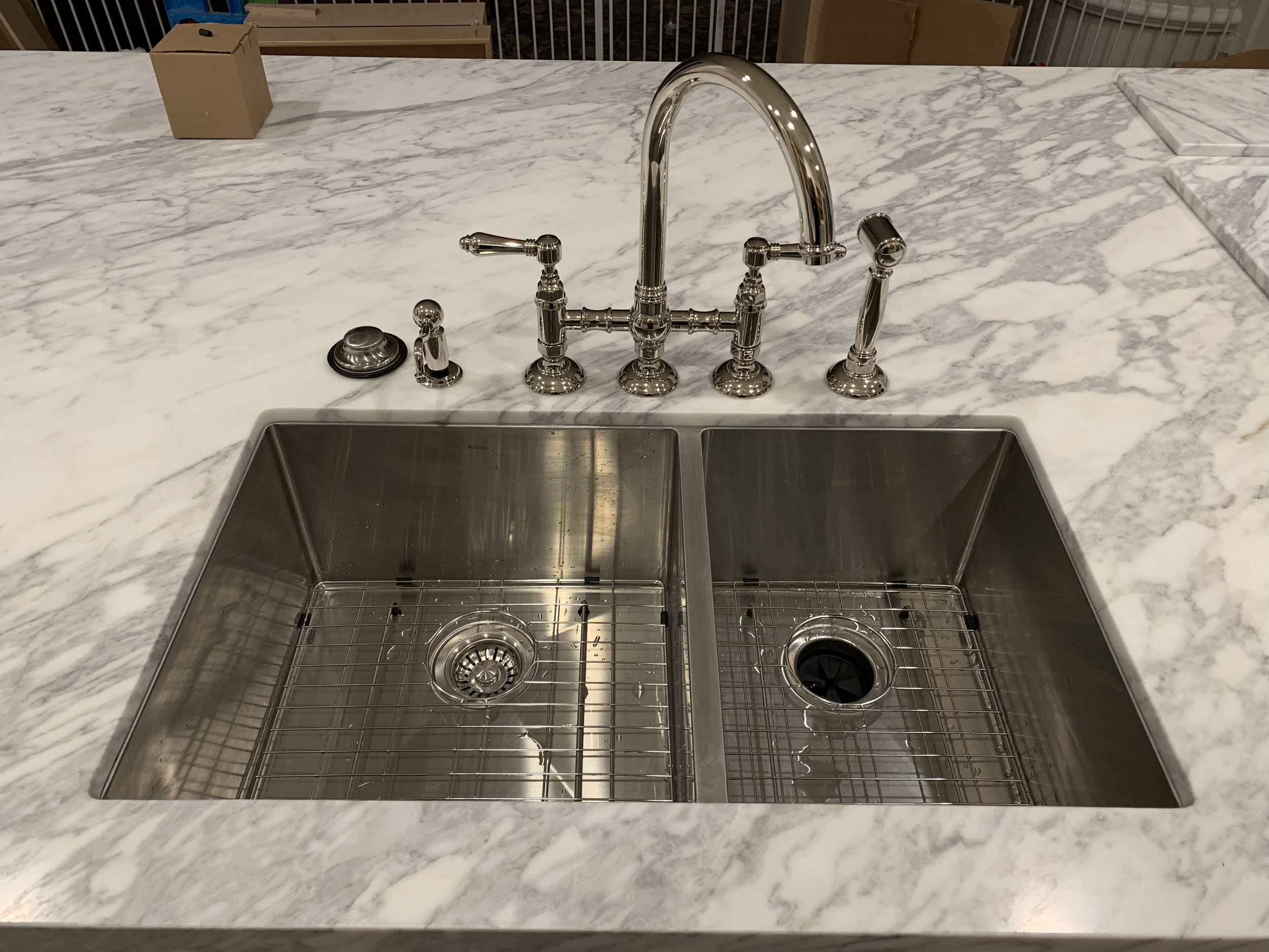 Stainless steel kitchen sink with two basins, on a white marble countertop with gray veining, and a chrome faucet.