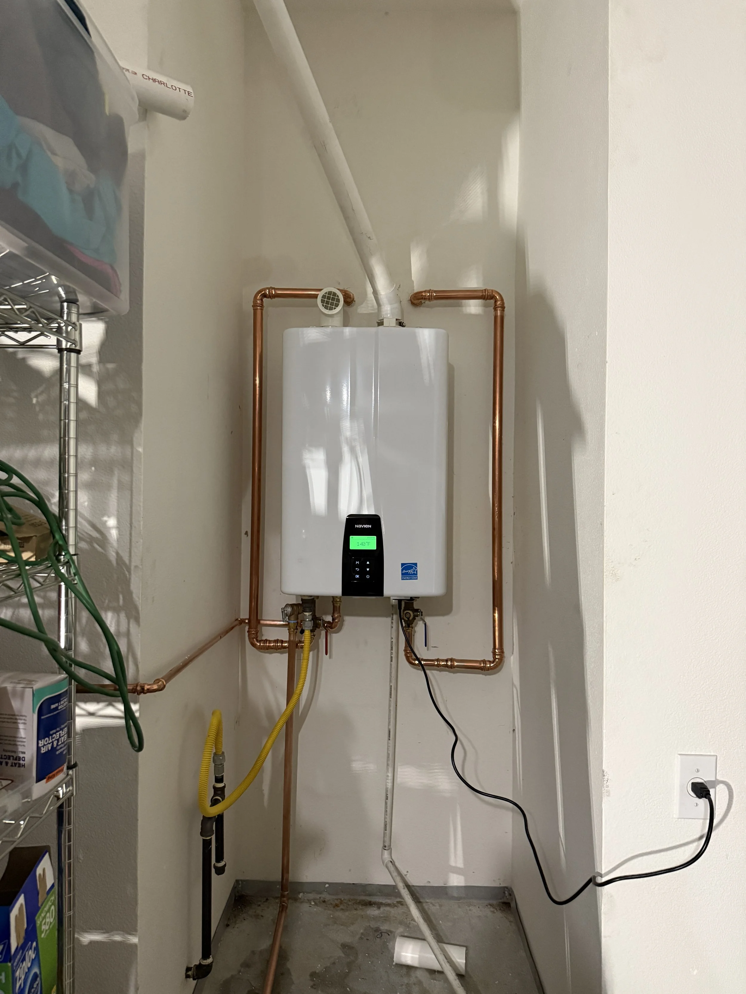Navien NPE-240 Tankless natural gas water heater with copper pipes, electrical wiring, and a digital display in a utility closet.