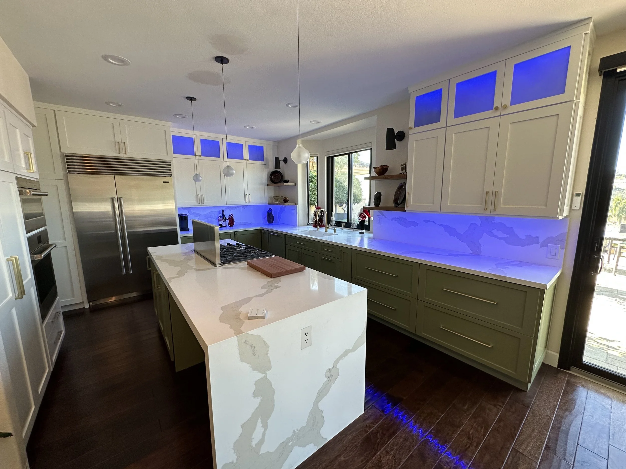 Modern kitchen with white and green cabinets, marble countertops, stainless steel appliances, and blue LED lighting.
