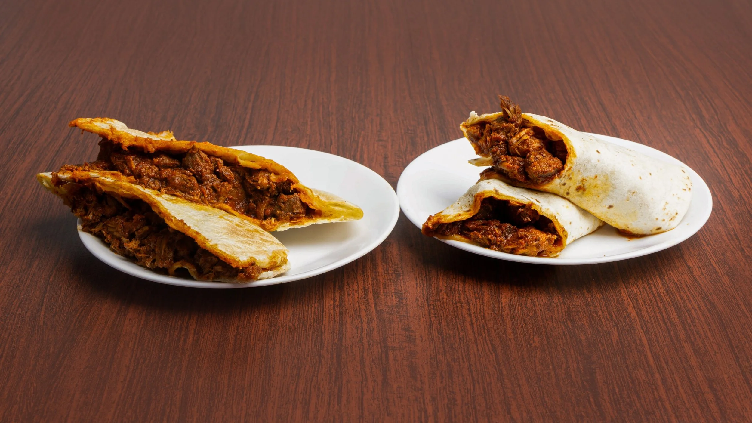 Two plates with beef burritos on a wooden table, one sliced open revealing beef filling.