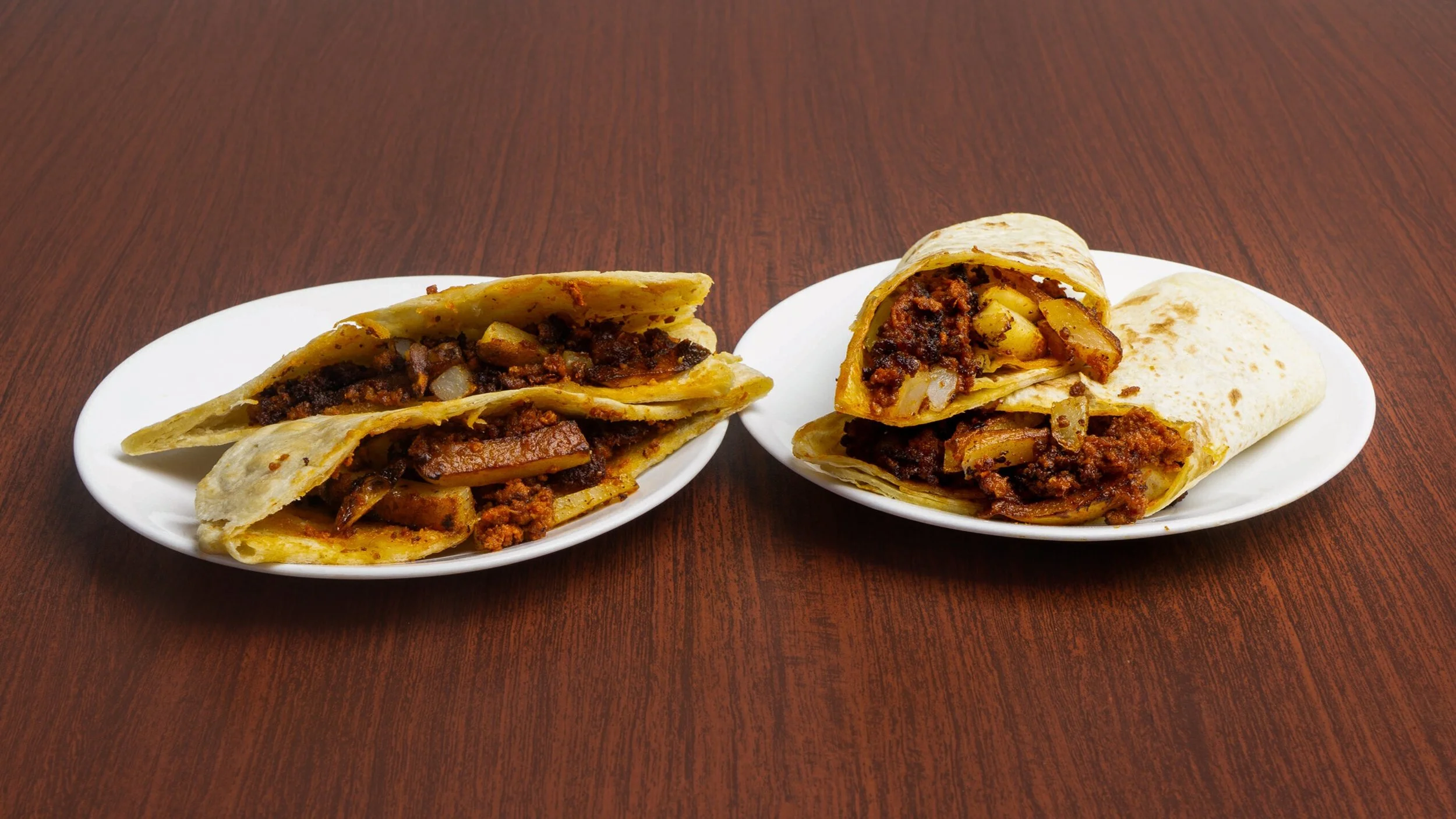 Two plates with beef taco wraps on a wooden table.
