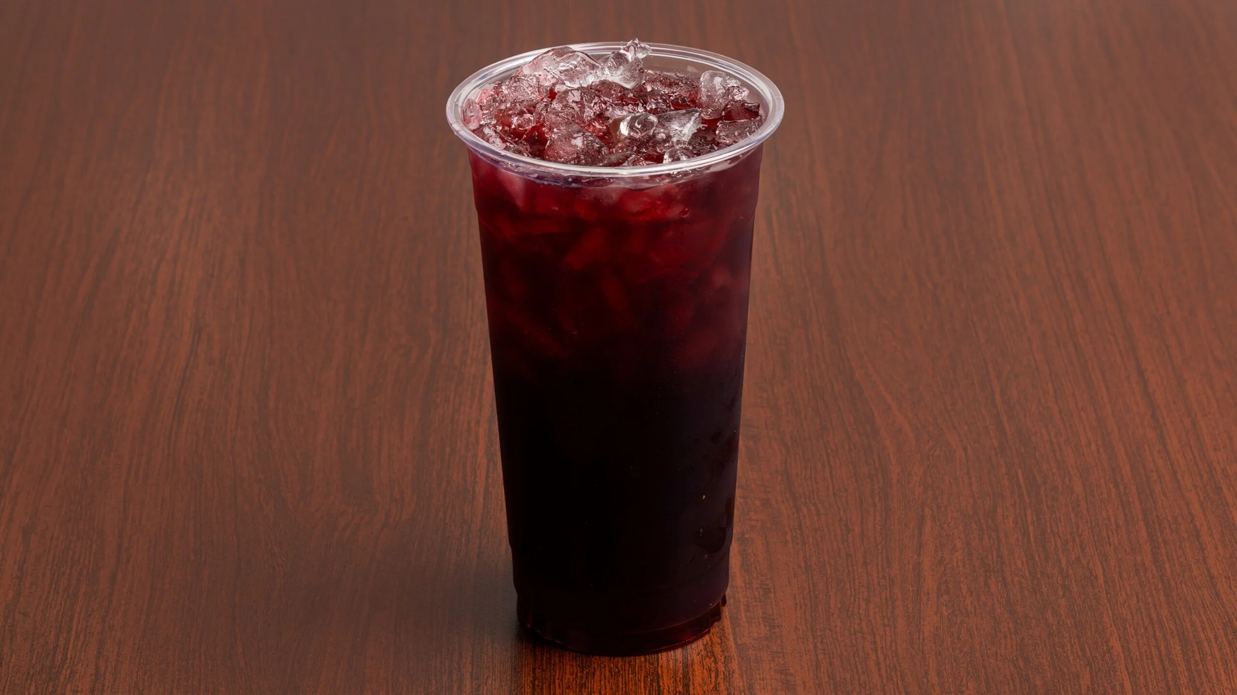 A plastic cup filled with a dark beverage and ice, placed on a wooden surface.