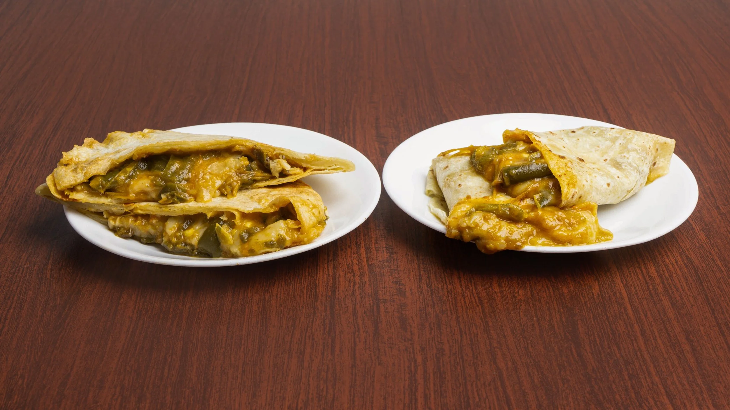 Two plates of breakfast burritos filled with cheese, green peppers, and other ingredients on a wooden table.