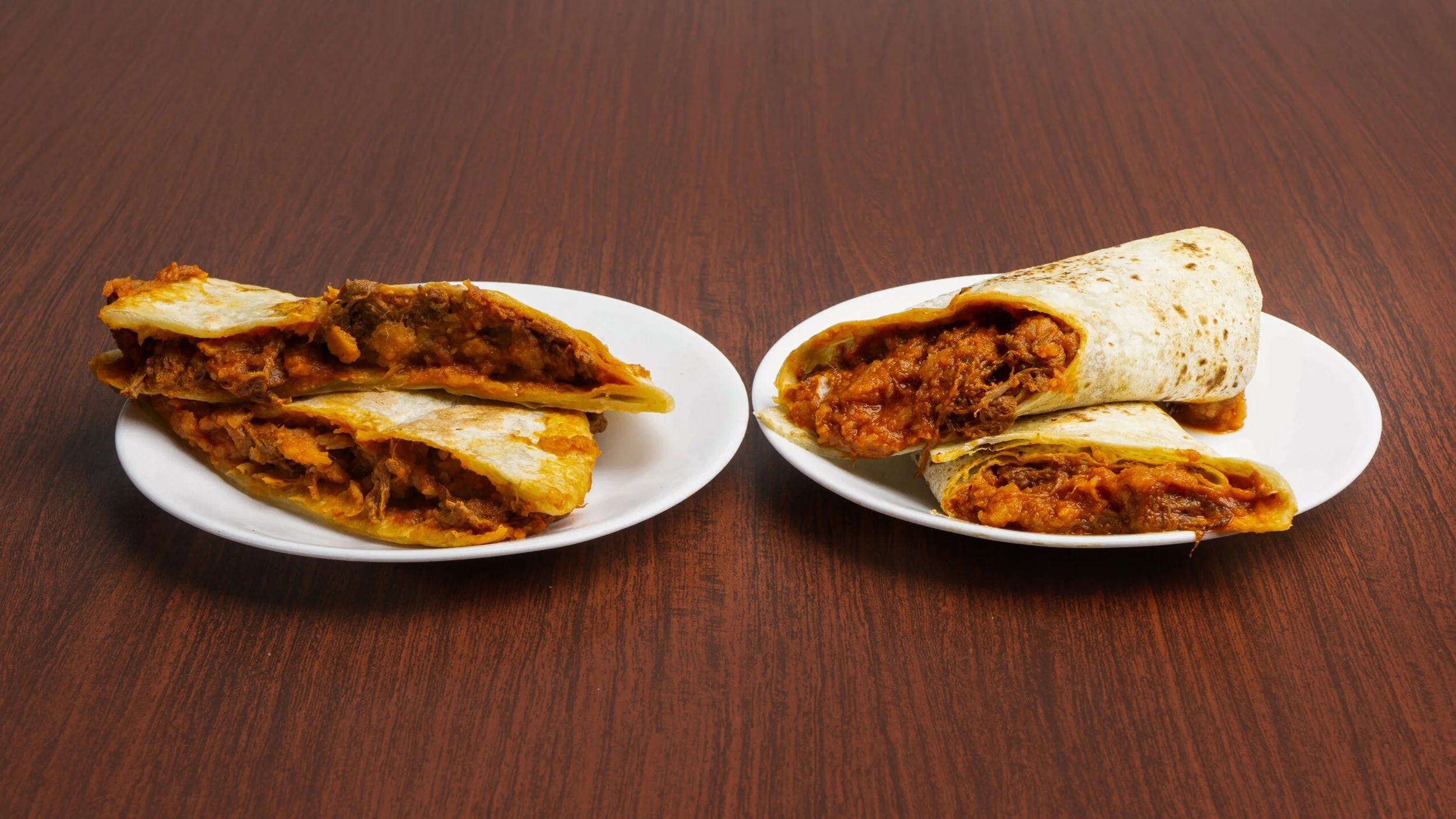 Two plates of beef and beans burritos on a wooden table.