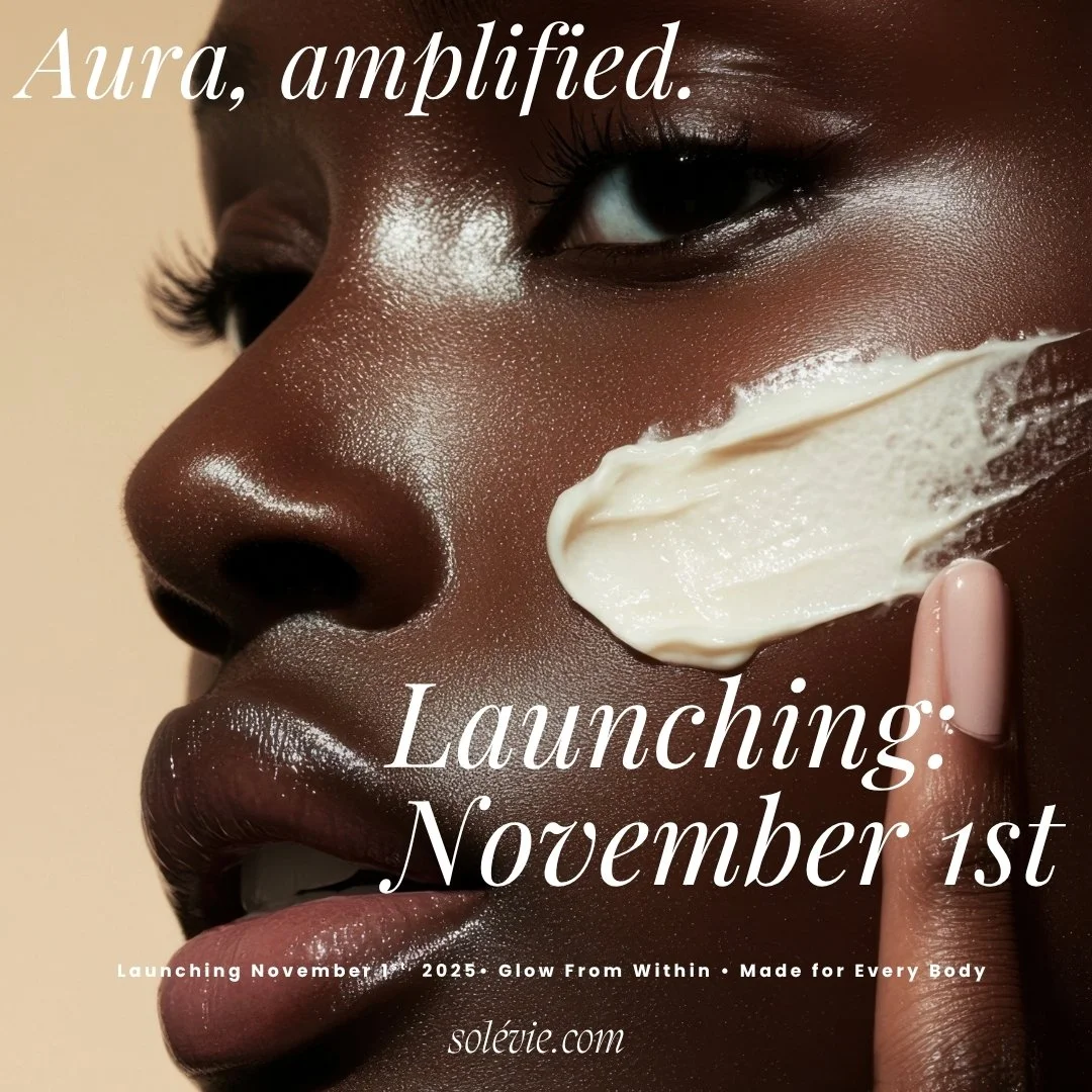 Close-up of a dark-skinned woman with glossy skin, applying white cream to her face, with text promoting a product launch on November 1st.