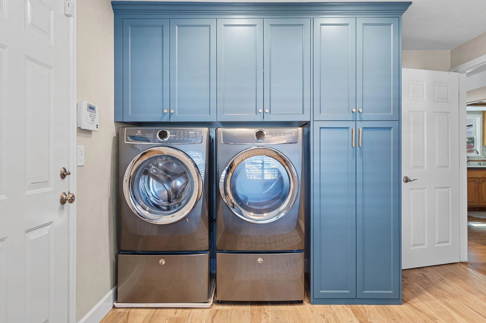 A Navy laundry room washer/dryer storage unit with two overhead cabinets and large side cabinet for hidden vacuum charging station and large item storage. 