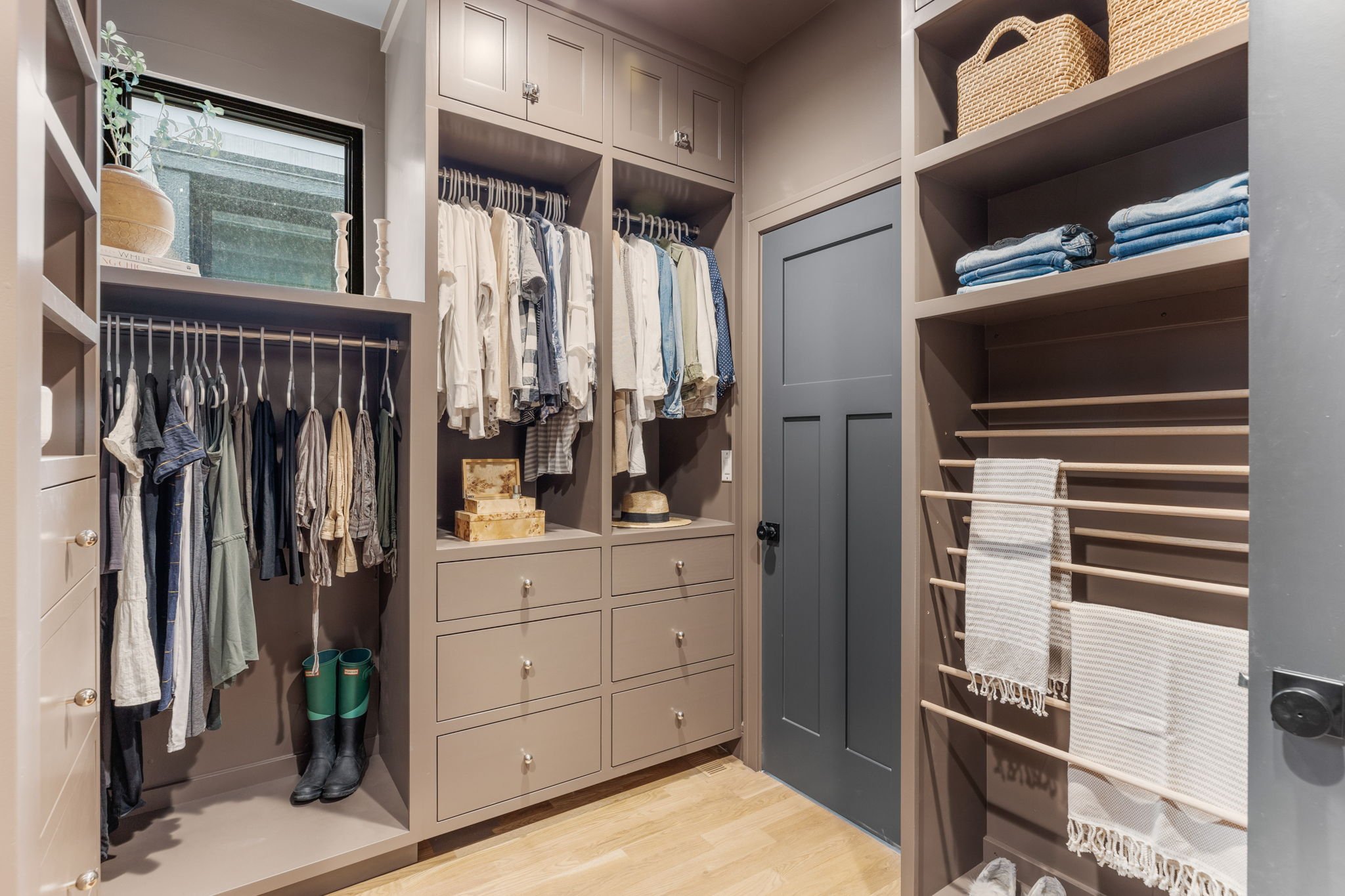 Closet with hanging clothes, shelves with folded towels, a drawer unit, and storage baskets.
