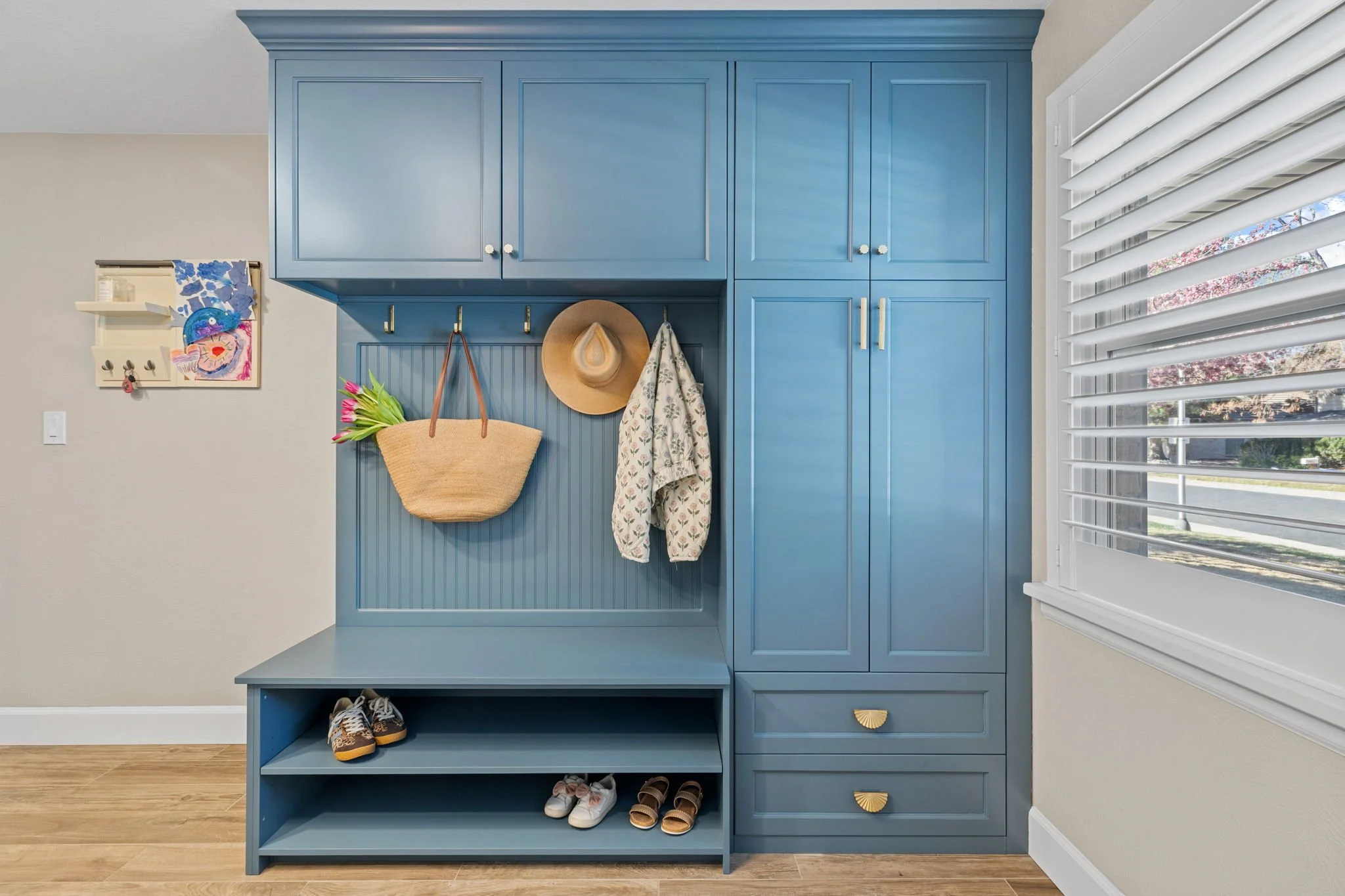 A Navy laundry bench unit with show rack integrated bench, wainscotting backed coat rack, and four-piece storage consisting of three cabinets with doors and a double drawer cabinet. 