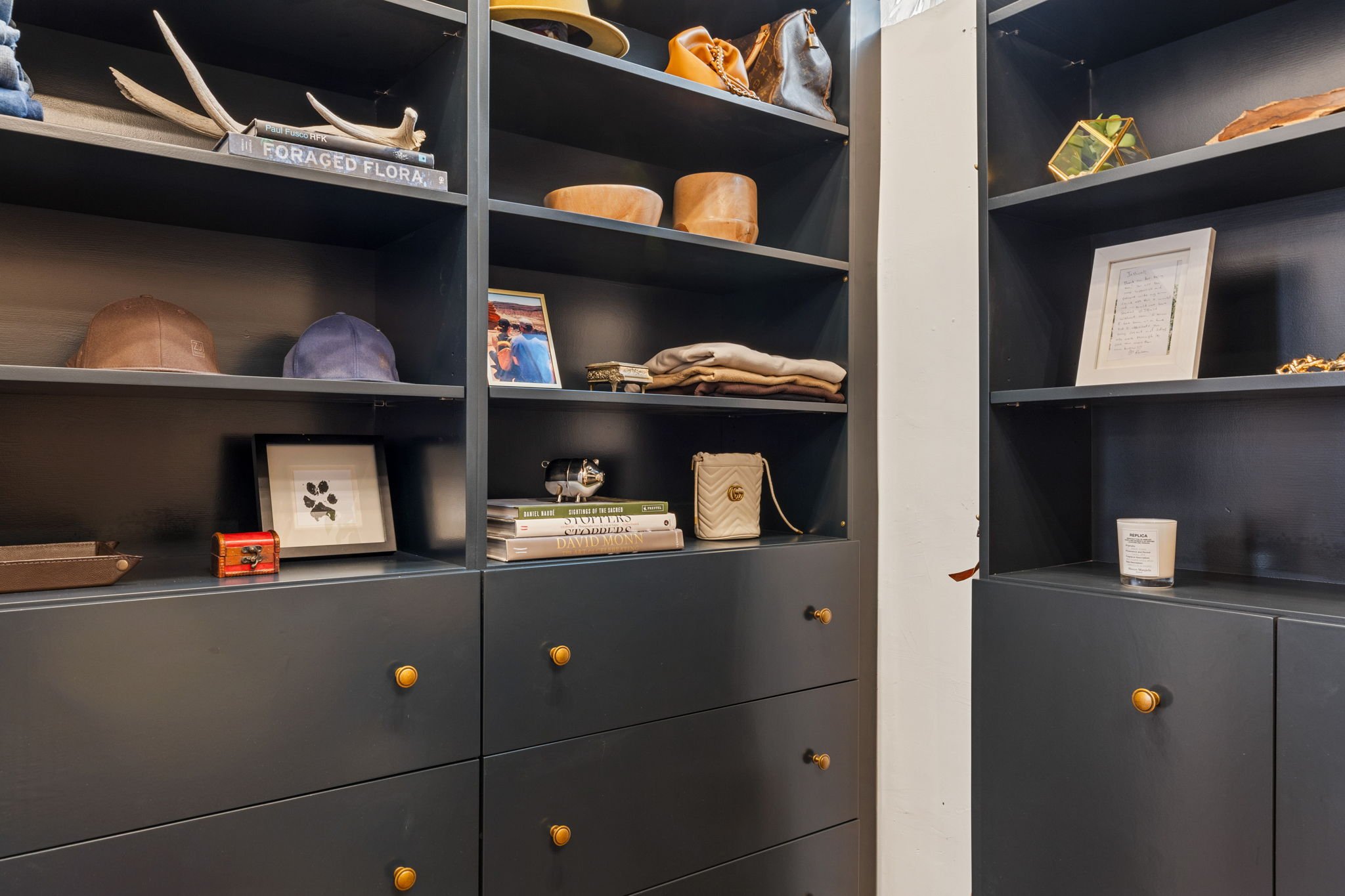 Black shelving units with various decorative items including hats, books, framed pictures, handbags, and a candle.