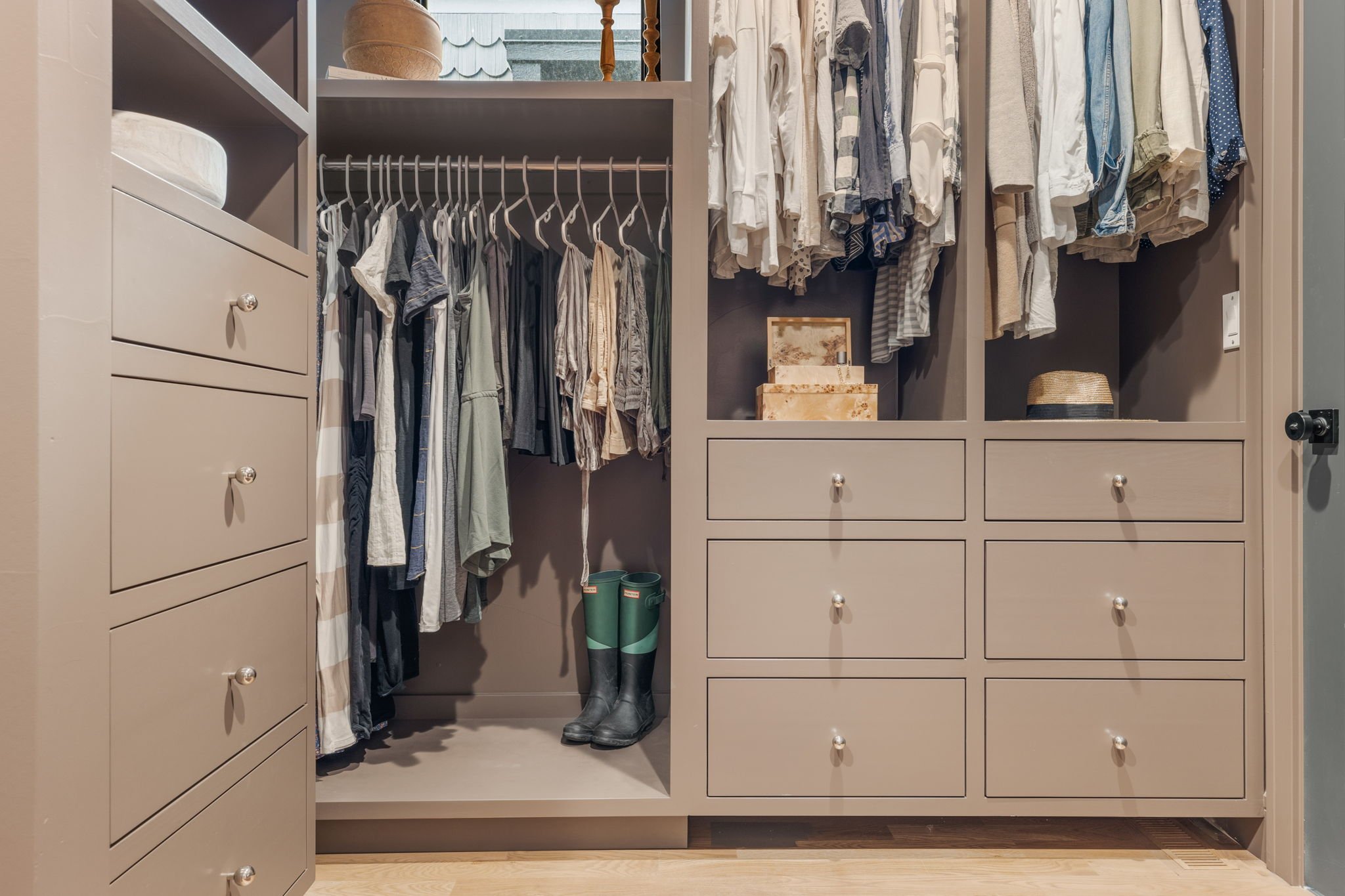 Organized walk-in closet with hanging clothes, drawers, and shelves, with boots and storage boxes visible.