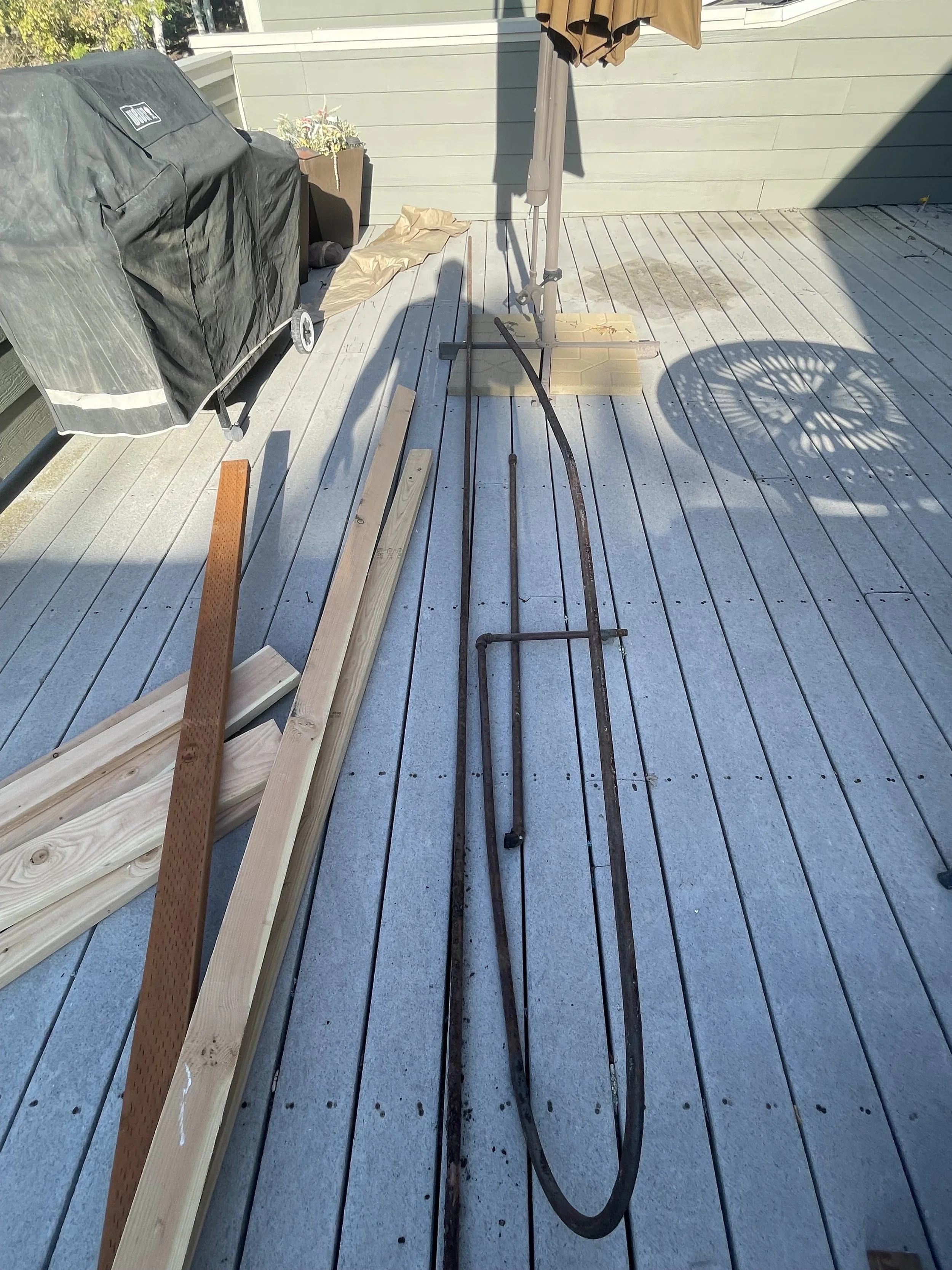 Outdoor deck with wooden planks, tools, and construction materials, including rusted metal rods, wooden beams, and a large black grill cover.