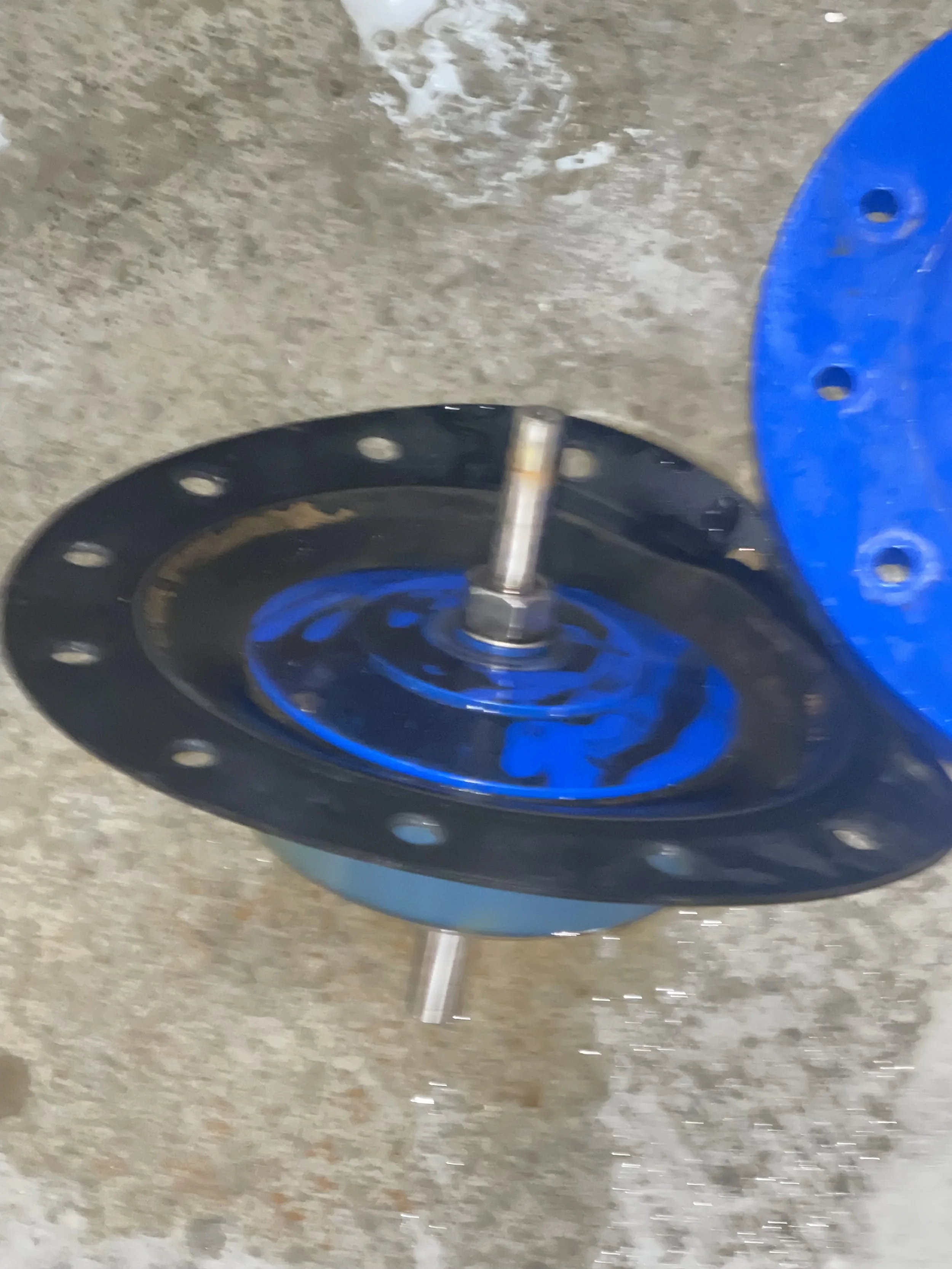 Close-up of a blue and black metal wheel or hub with a silver axle, lying on a concrete floor.
