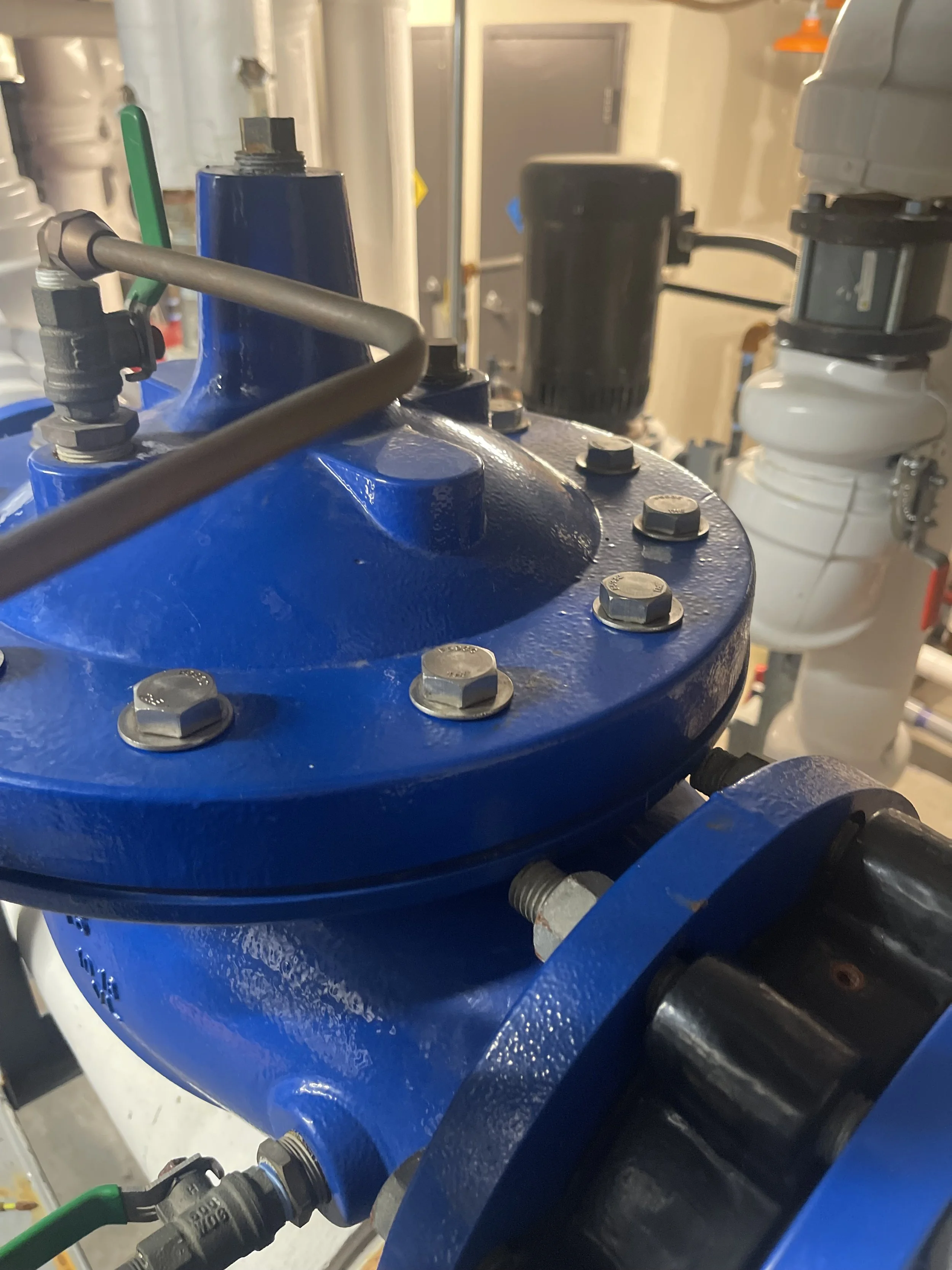 Close-up view of a blue industrial valve with bolts, connected to pipes and equipment in a mechanical or industrial setting.