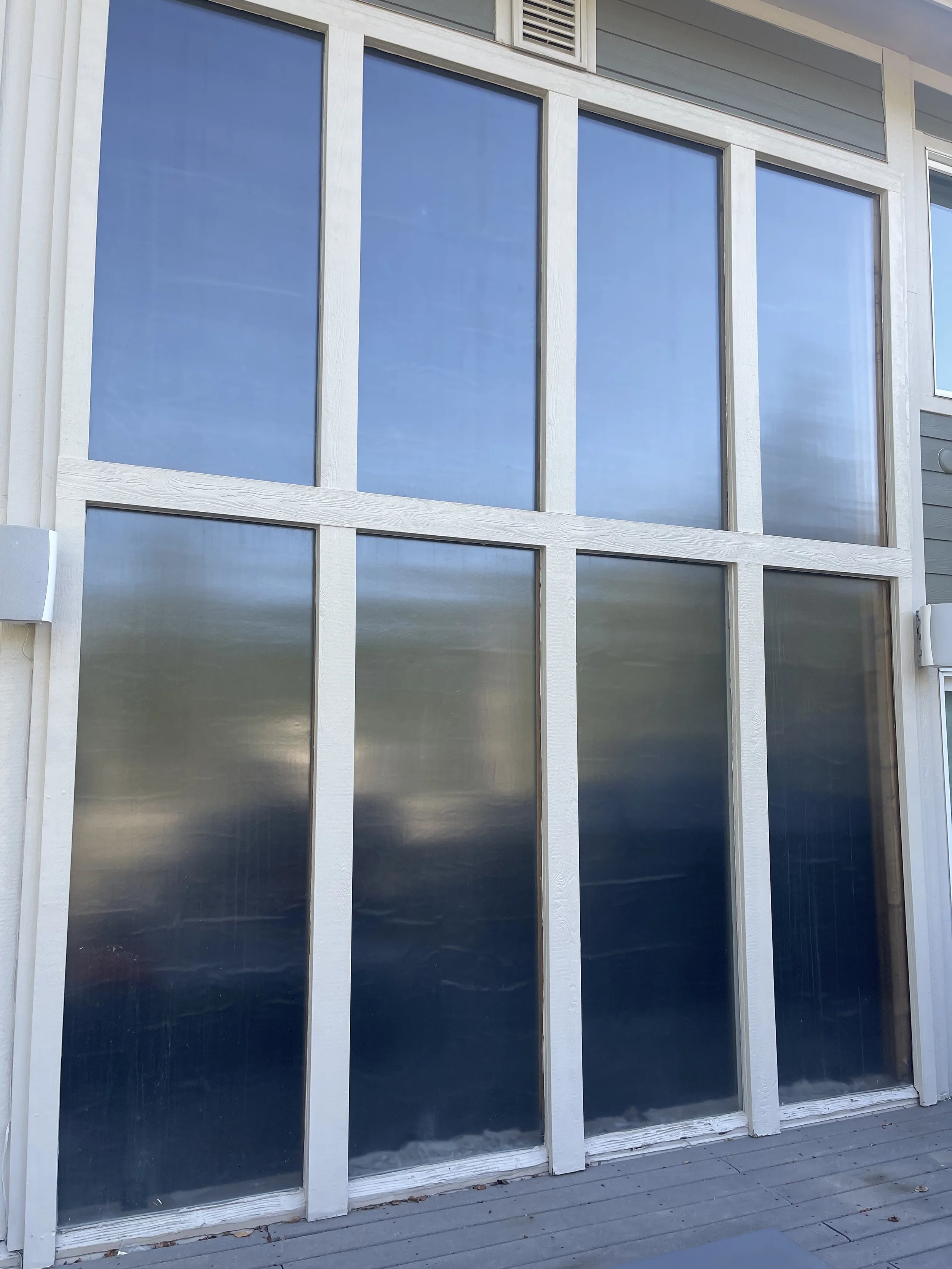 Large glass windows on the exterior of a building, with some windows reflecting the sky and clouds.