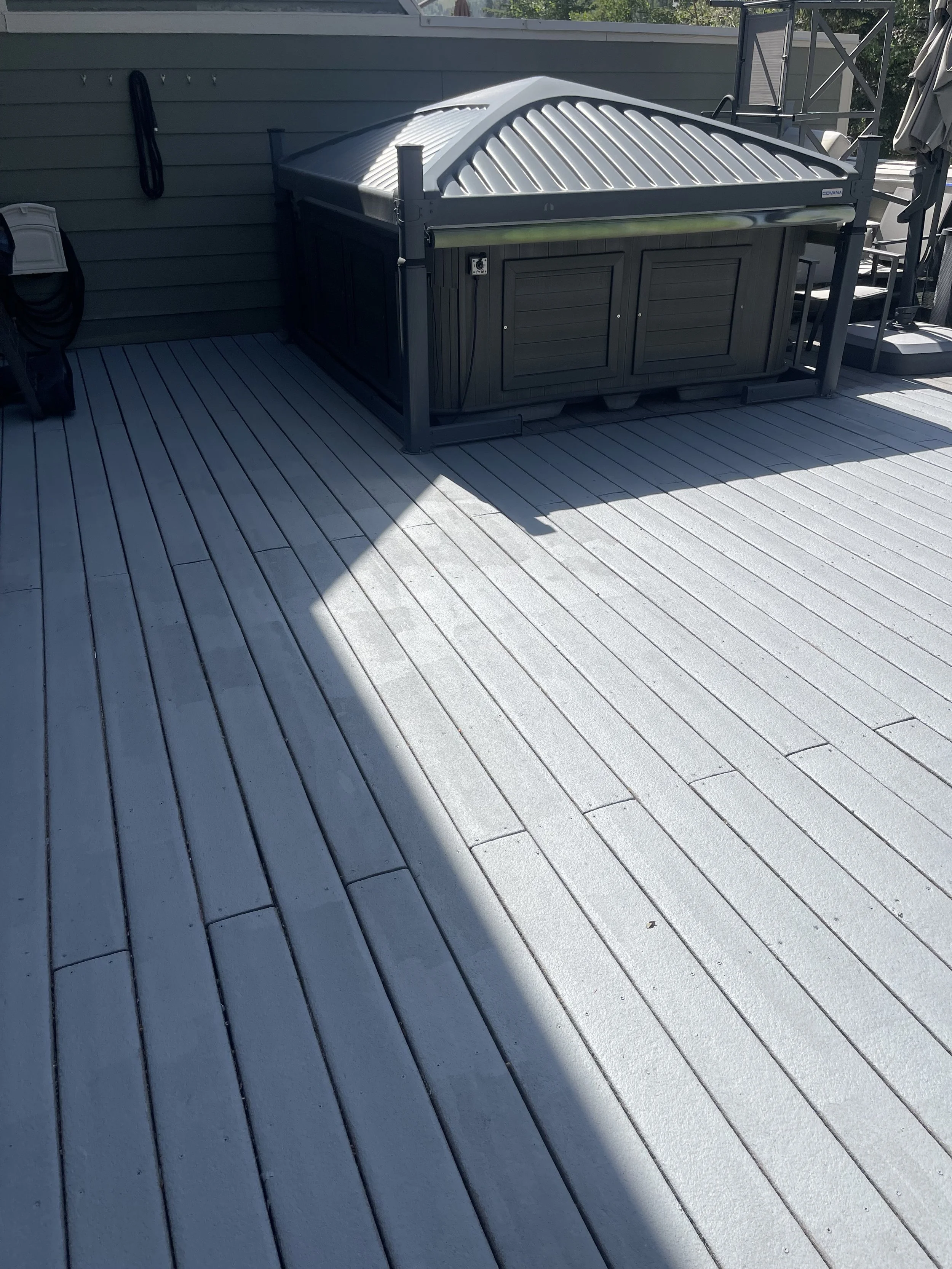A wooden deck with a hot tub built into the corner, and a shaded area casting a shadow over part of the deck.