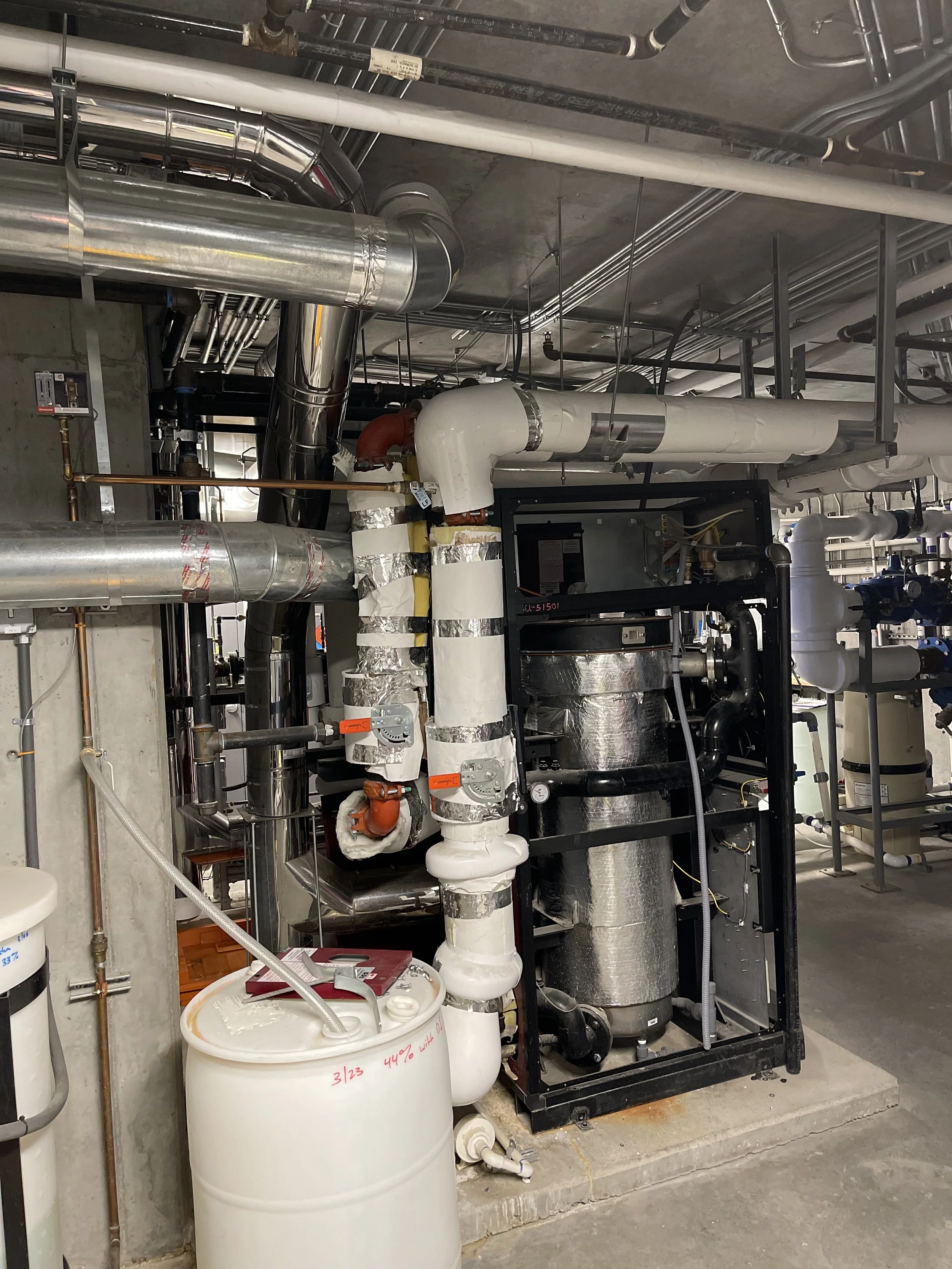 Industrial HVAC system with metal pipes, insulation, and mechanical equipment in a basement or utility room.