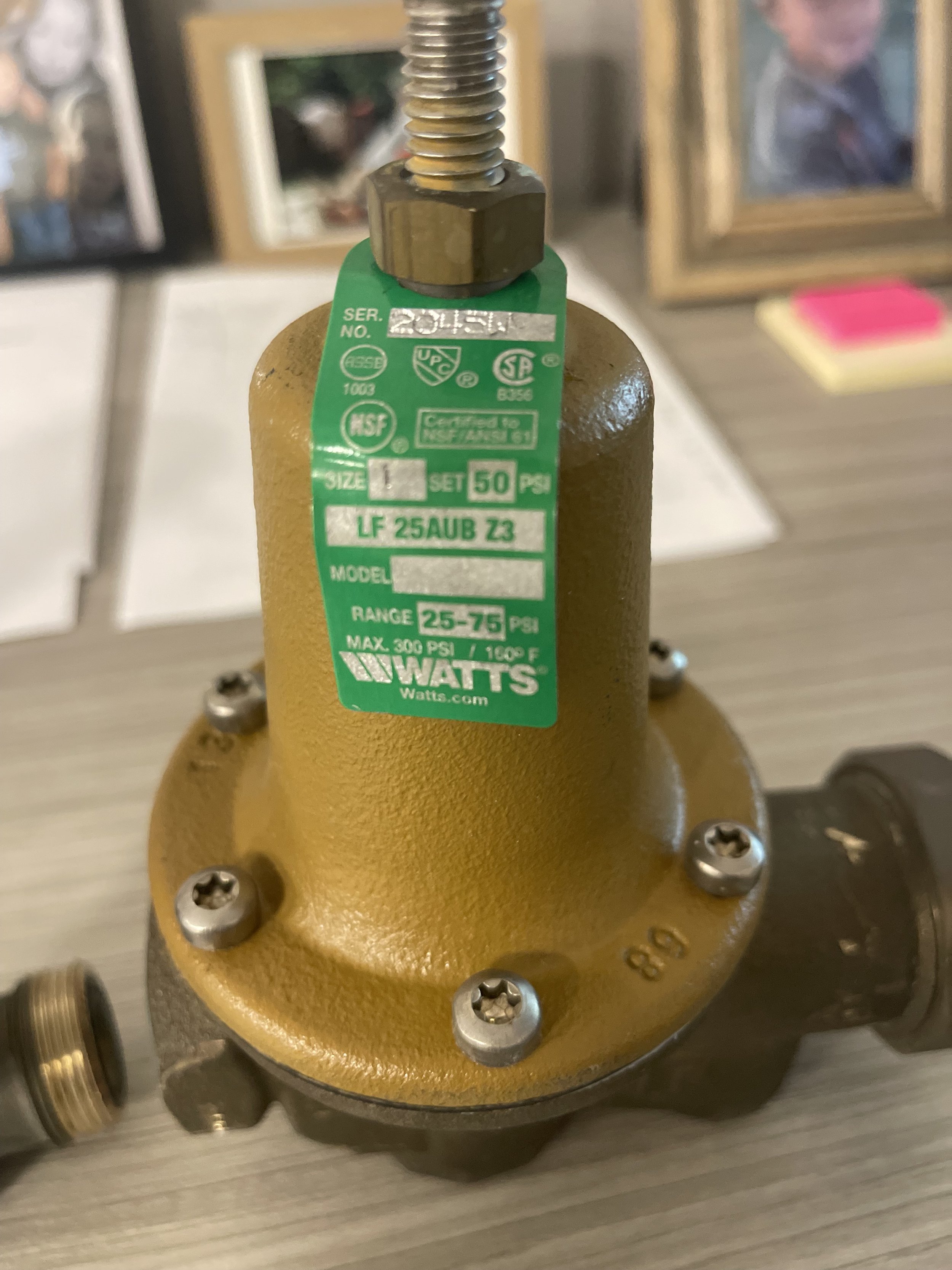 A yellow industrial valve with a green certification tag on top. The tag displays specifications including size, pressure range, and model number, with some other components partially visible around it.