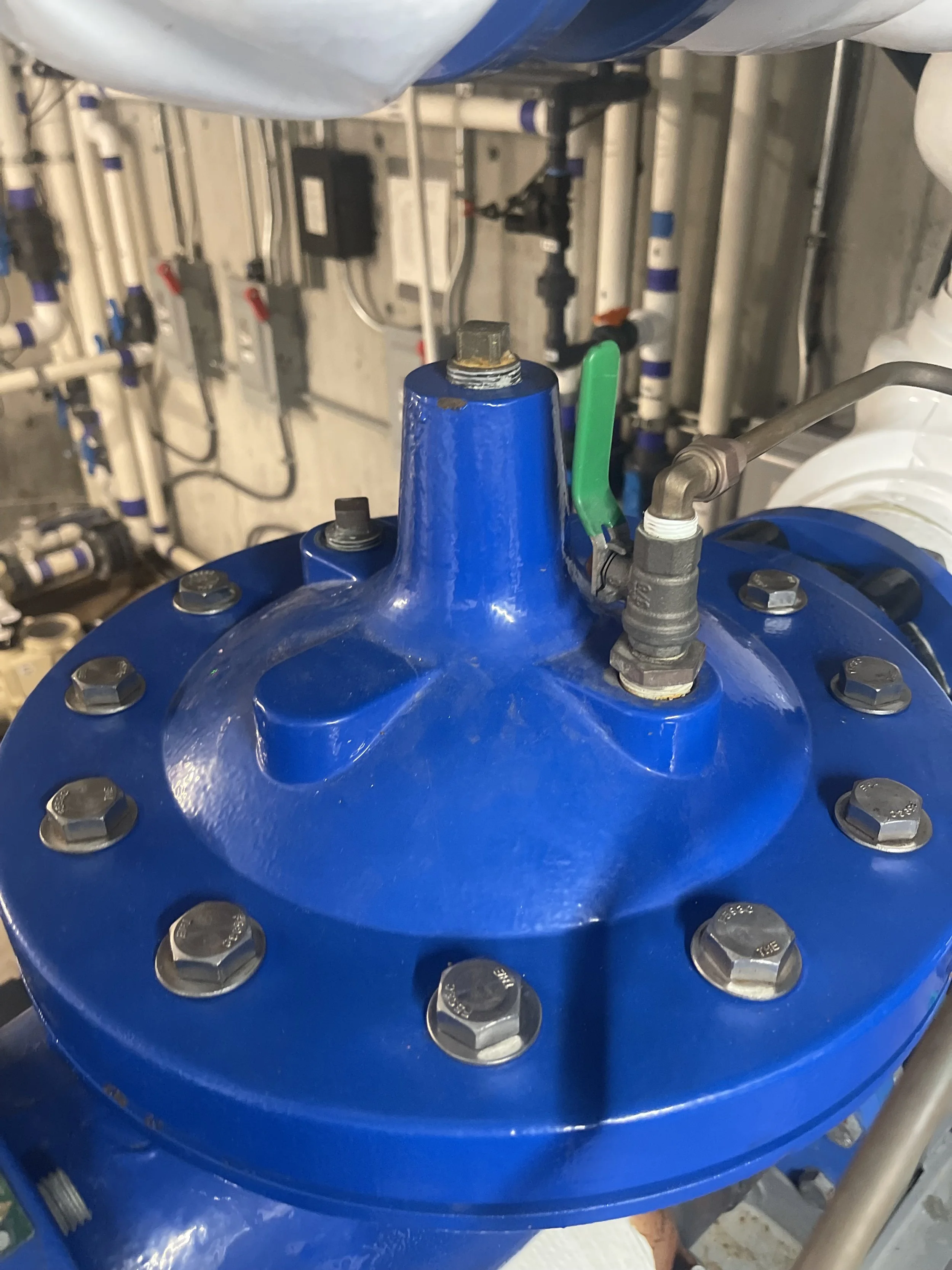 A large blue industrial valve with a green handle, bolted onto a pipe system in a mechanical room.