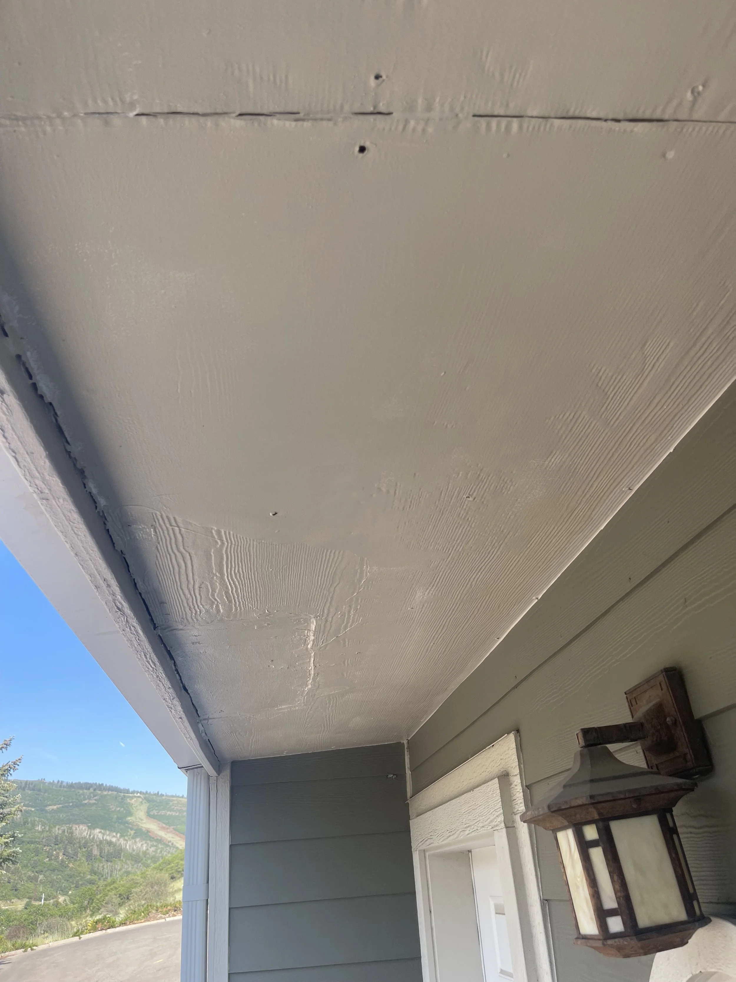 Exterior porch ceiling with textured beige paint, green painted wall, and a wall-mounted outdoor lantern fixture.