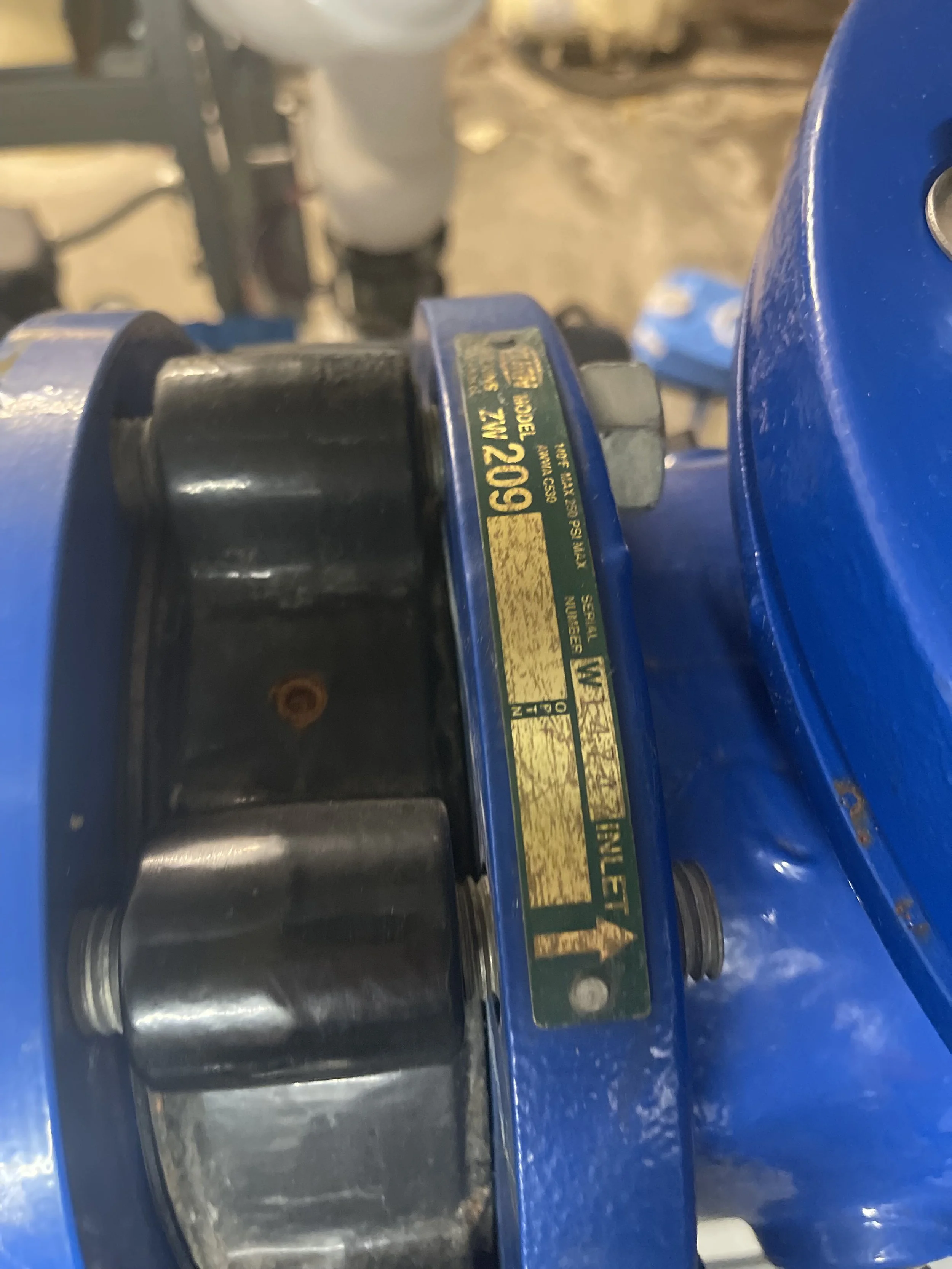 Close-up of a blue mechanical device with a yellow label, showing a black bolt and some rust.