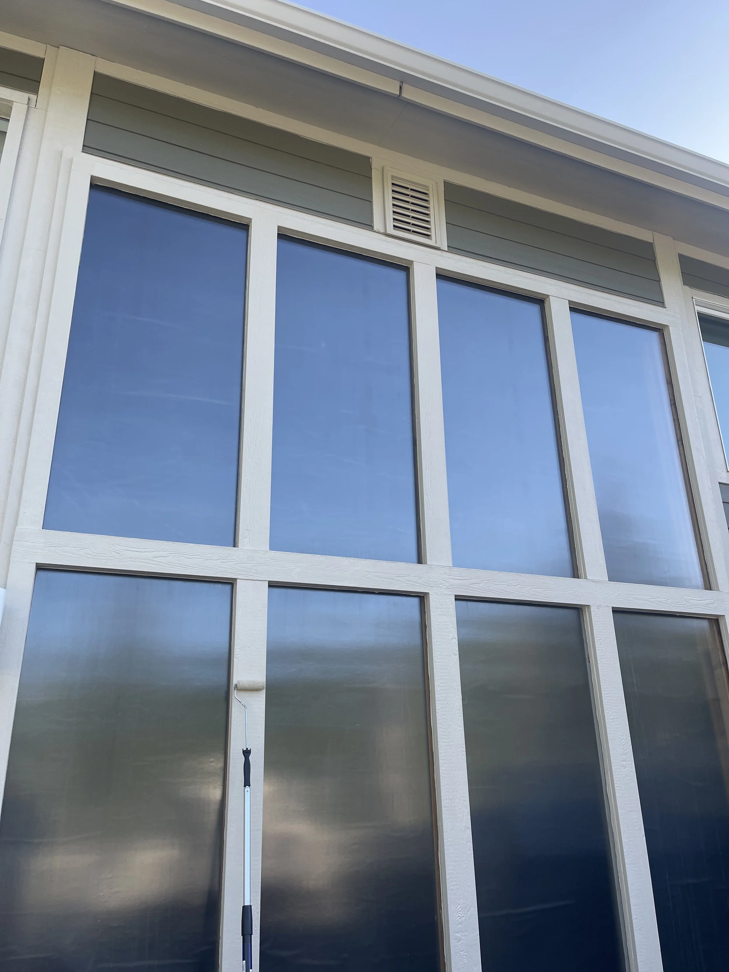 Close-up of a house's screened porch with large glass panels, white framing, and a small vent near the roof.