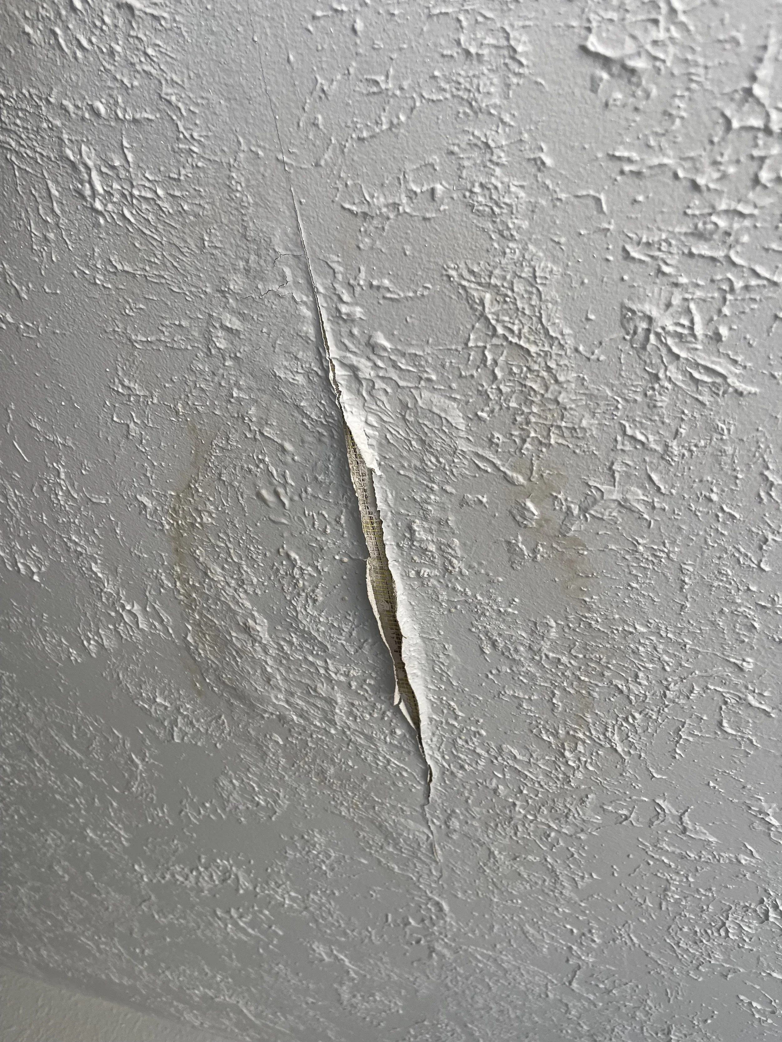 Close-up of a textured white ceiling with a long crack running through it.