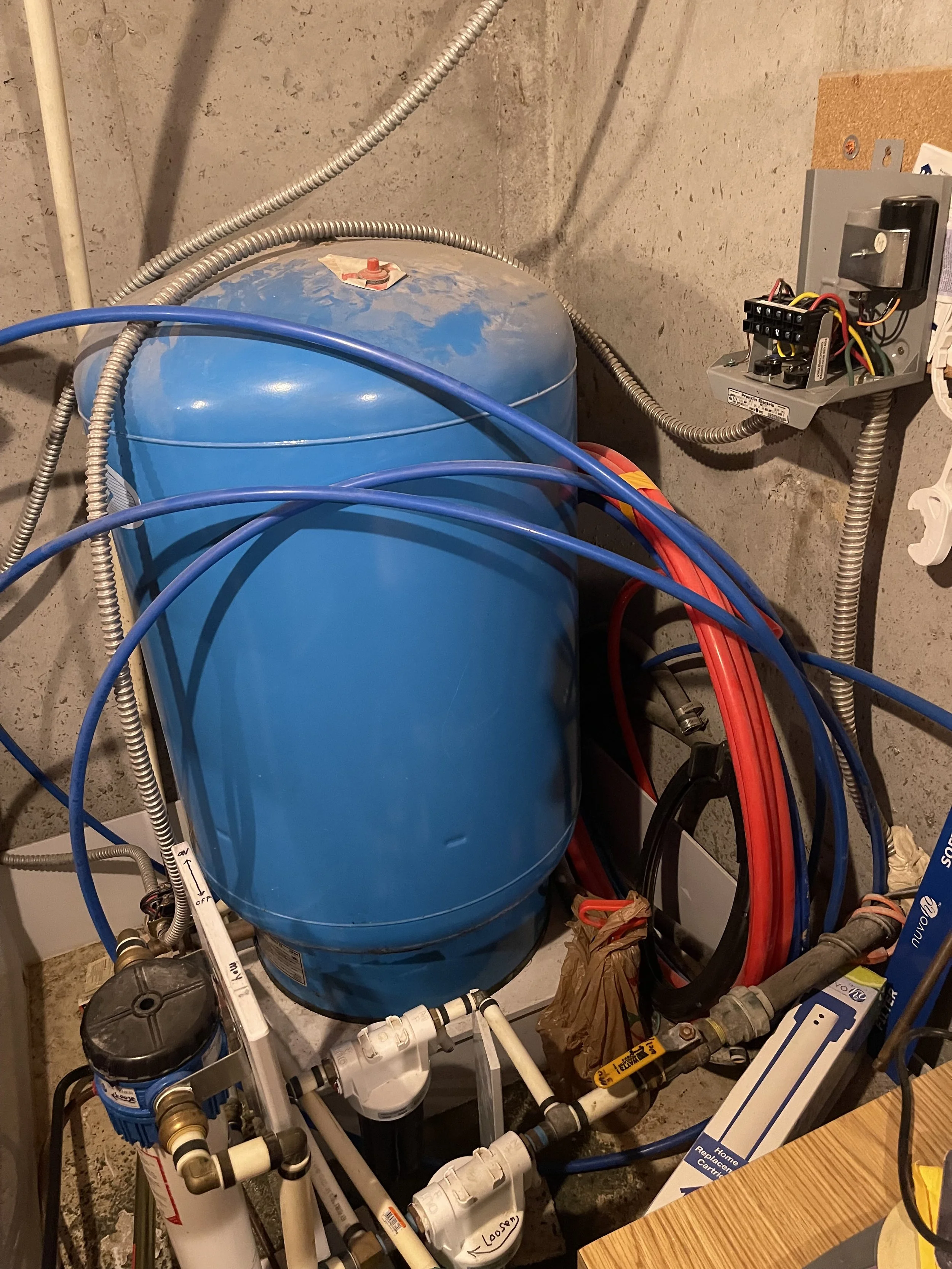 A blue water pressure tank connected to plumbing and electrical components in a basement or utility room.