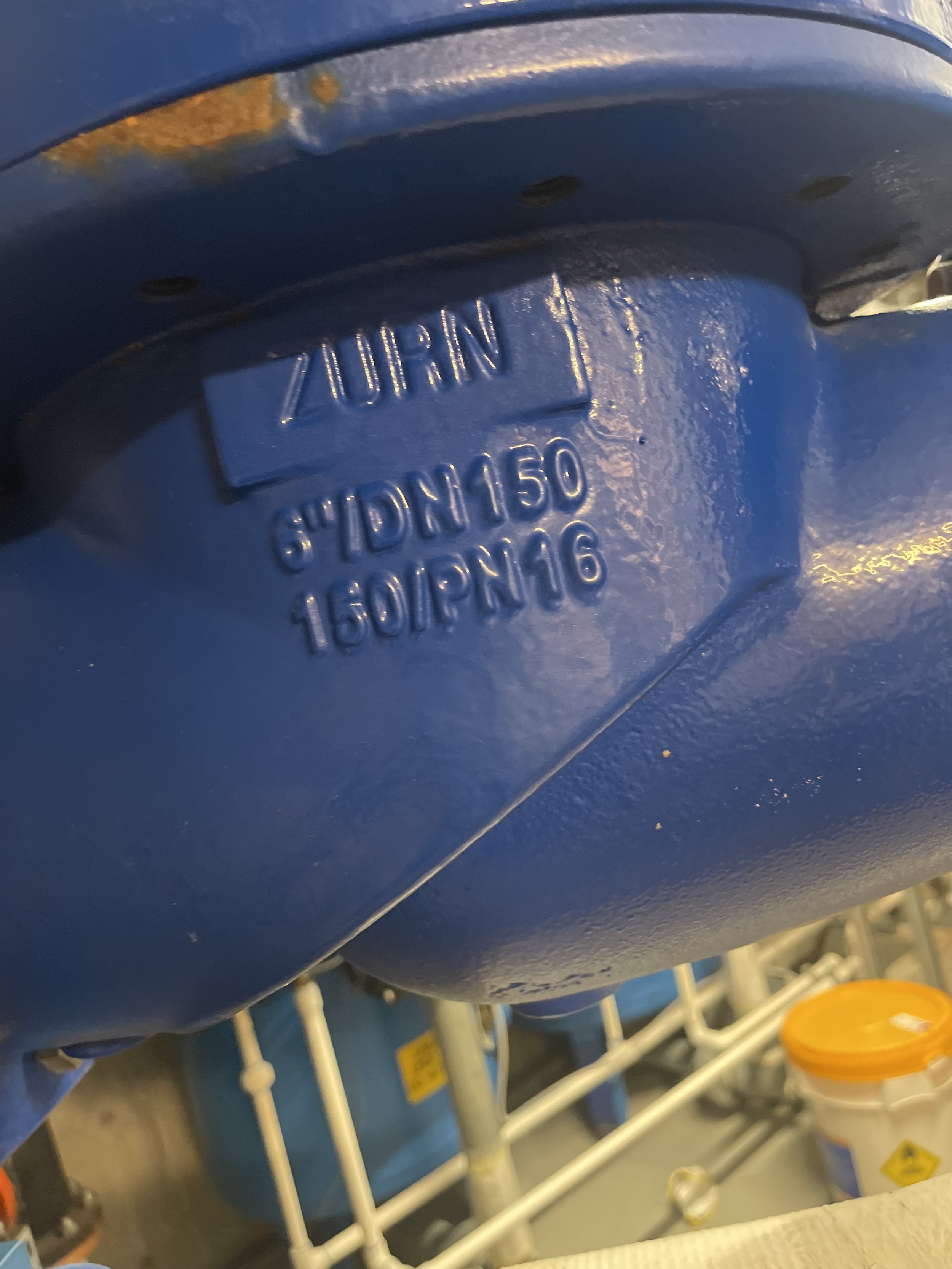 Close-up of a blue plastic container with embossed markings including the brand 'ZURN' and specifications 'SH'DN150' and '16.00/PN16'.