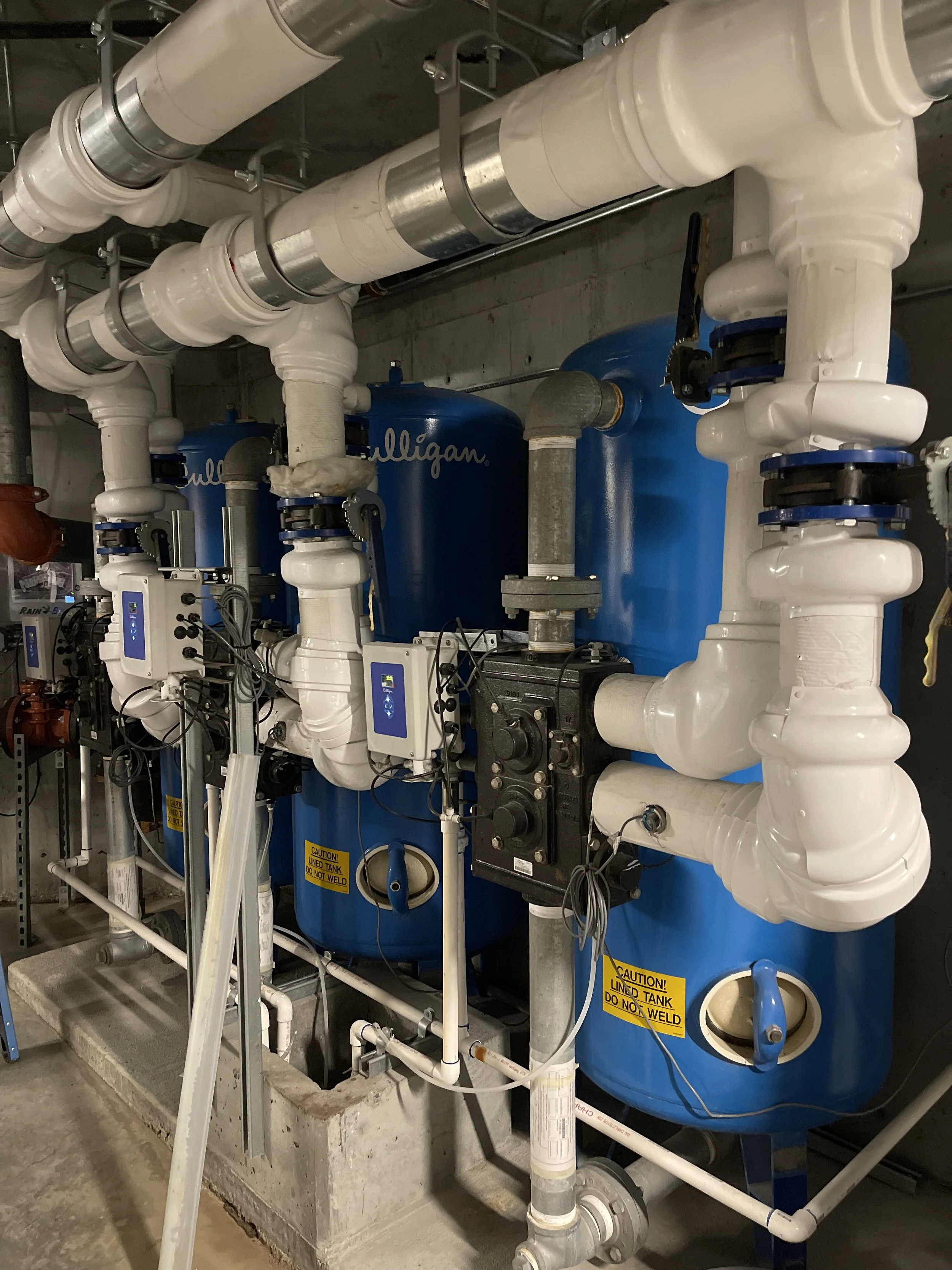 Industrial water treatment system with two large blue tanks labeled 'Culligan,' connected by white and gray pipes and control panels.