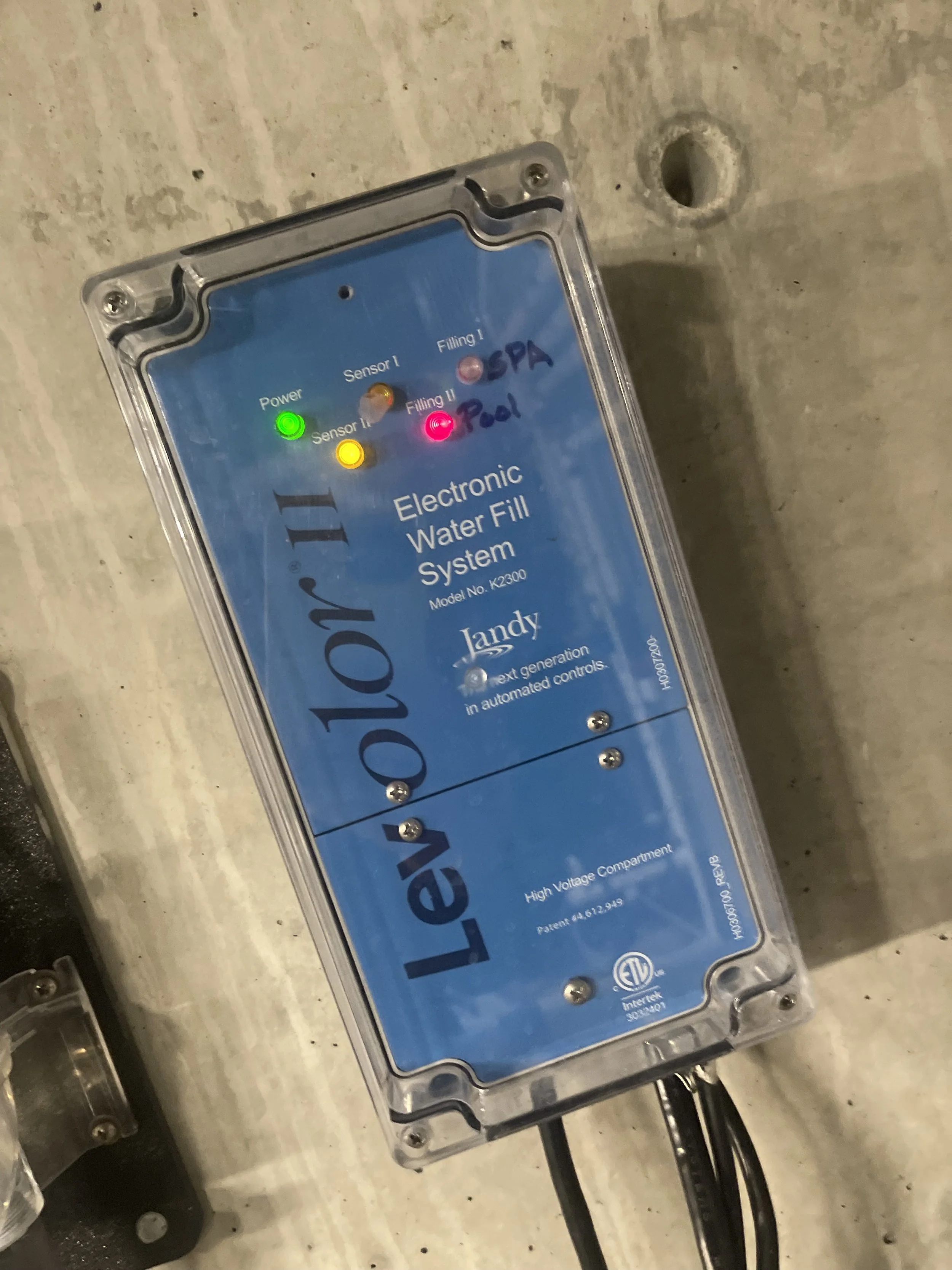 Electronic water fill system control box with indicator lights labeled Power, Sensor I, Sensor II, Filling I, Filling II, SPA Pool, and Pool, mounted on a concrete surface.