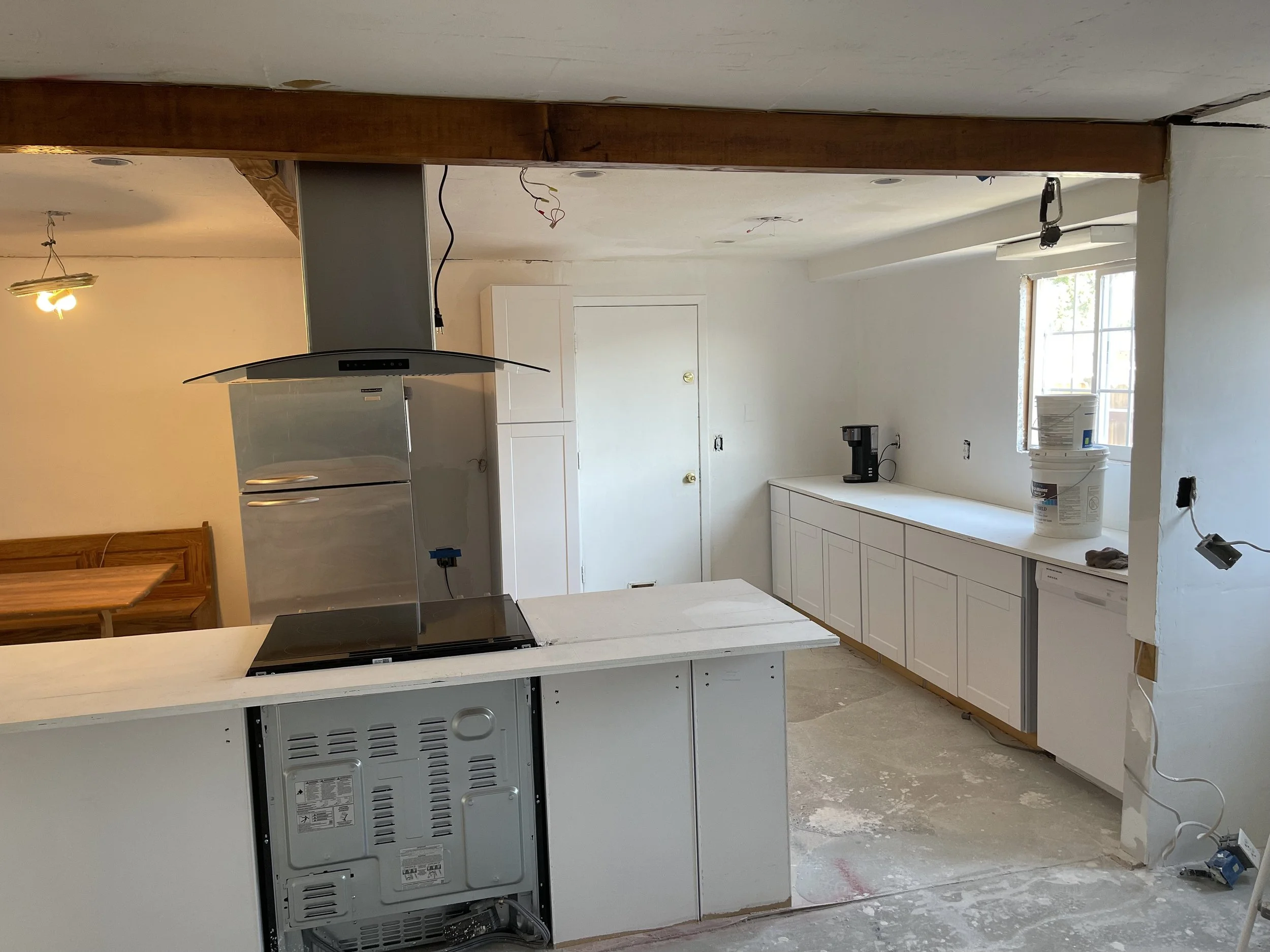 Kitchen under renovation with unfinished flooring, missing appliances, and exposed wiring.