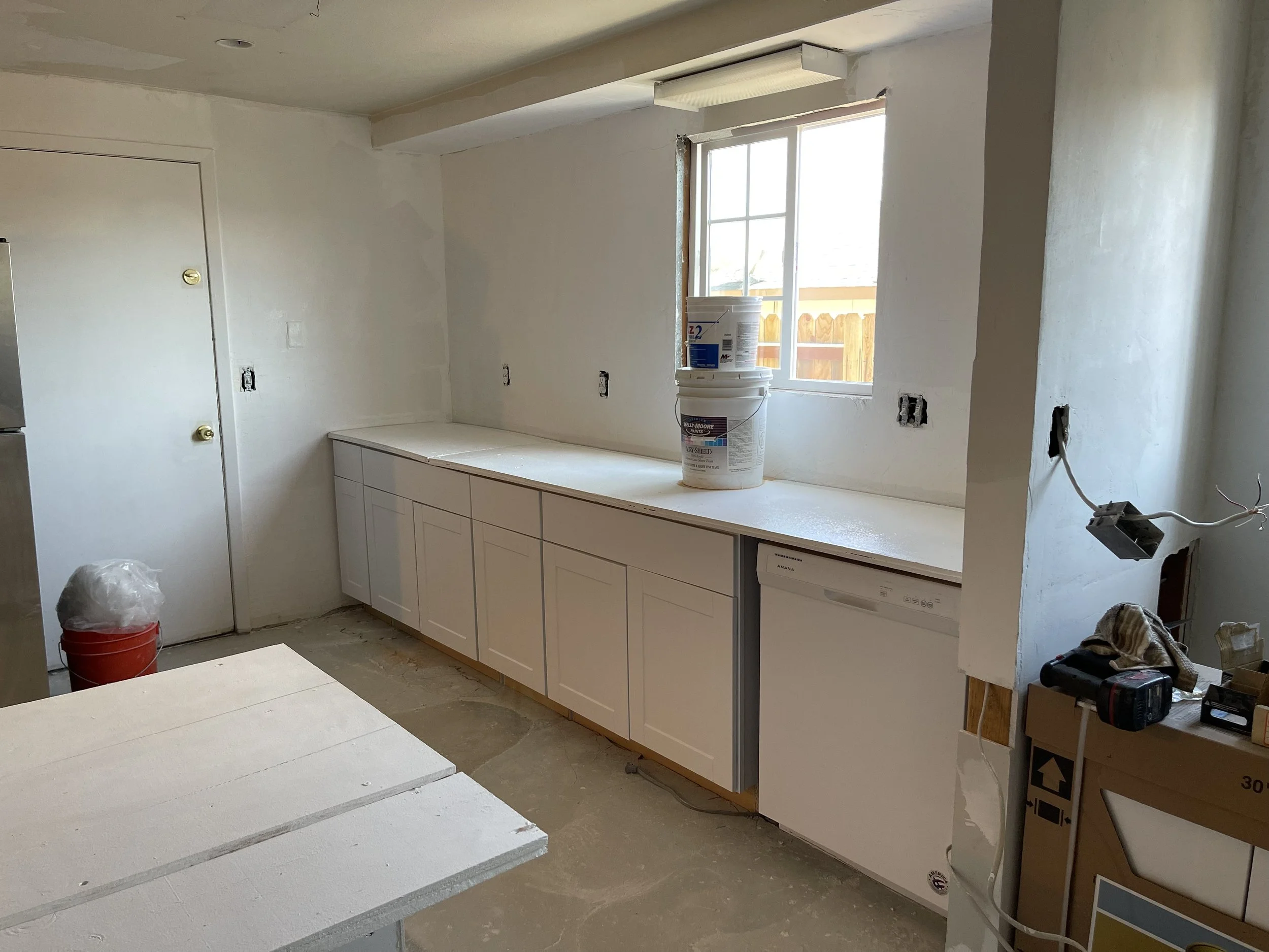 Kitchen under construction with white cabinets, a window, construction tools, and supplies.